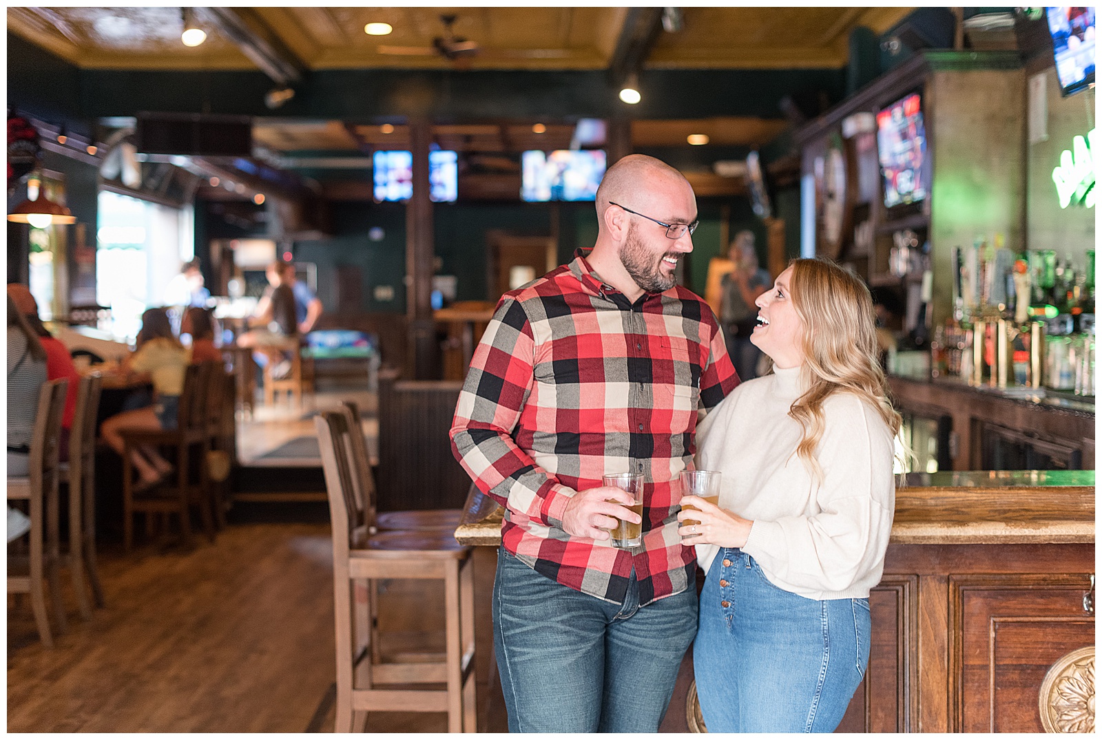 the couple is standing and leaning against the bar counter while holding their drinks and looking at each other and smiling with the guy on the left and the girl on the right and a tall chair is beside the guy in downtown Pittsburgh