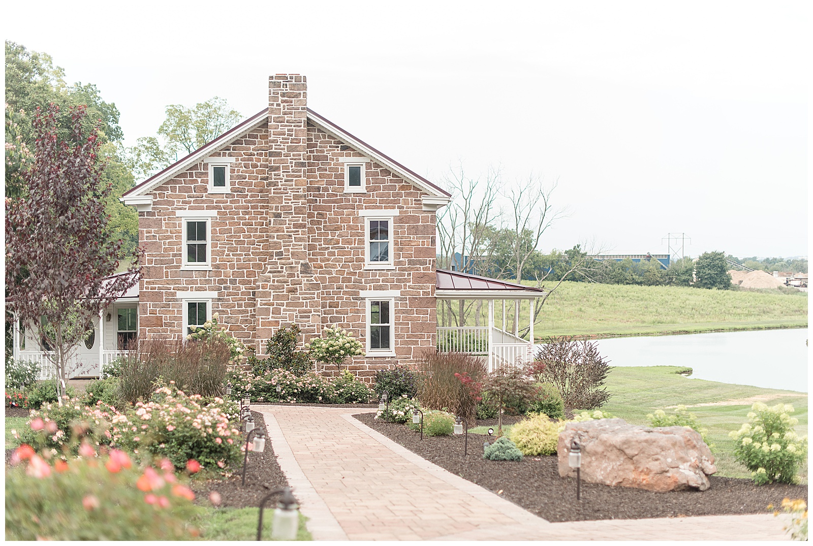 photo of the side of beautiful old sandstone farm house with front porch looking out over pond and landscaped walkway and flowerbeds leading towards house at Spring Valley Farms in Dover, PA