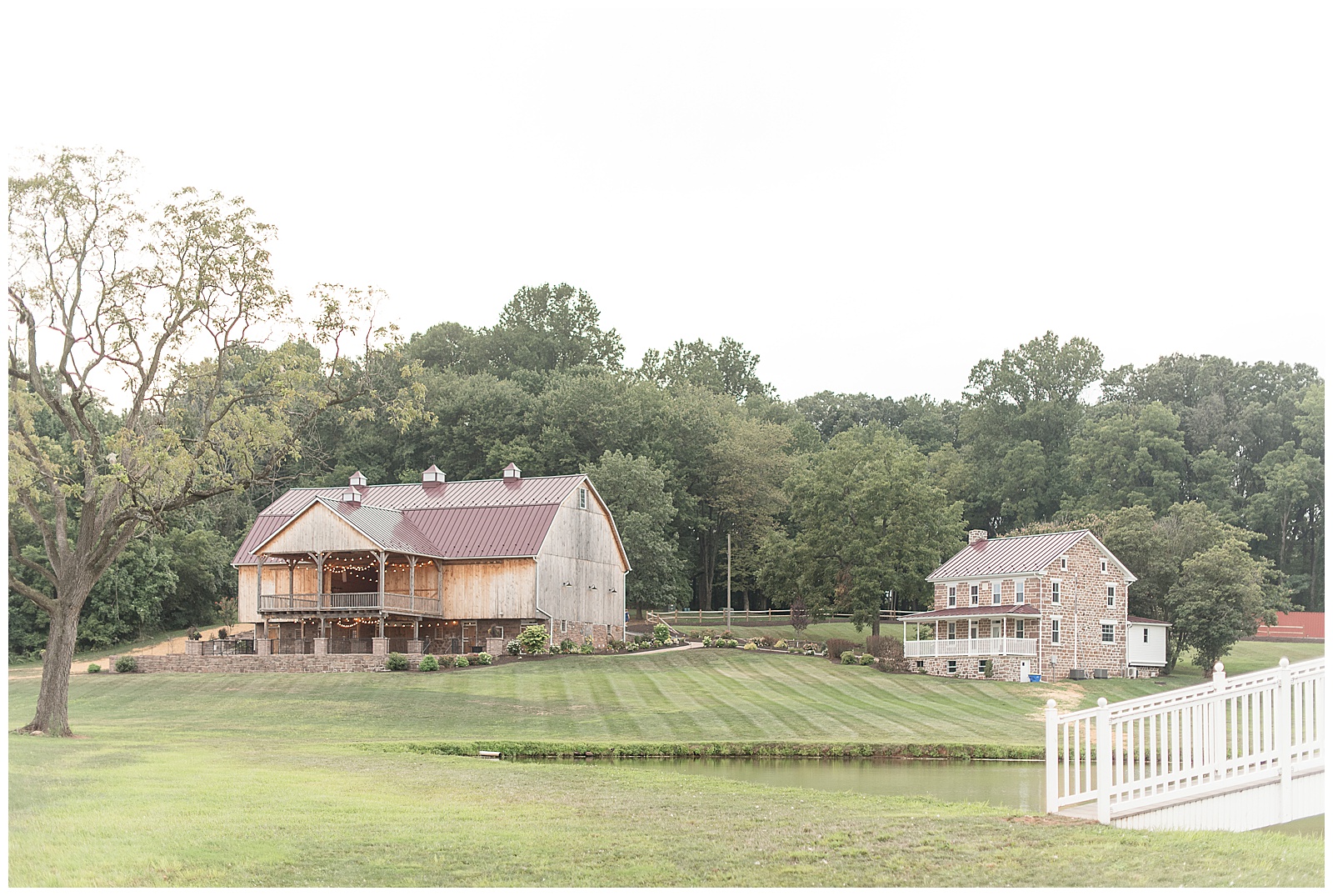 photo of rustic faded ivory barn on left side of property and large grass yard and pond and beautiful sandstone farmhouse on right side of photo with row of trees along the back of the photo at Spring Valley Farms in Dover, PA