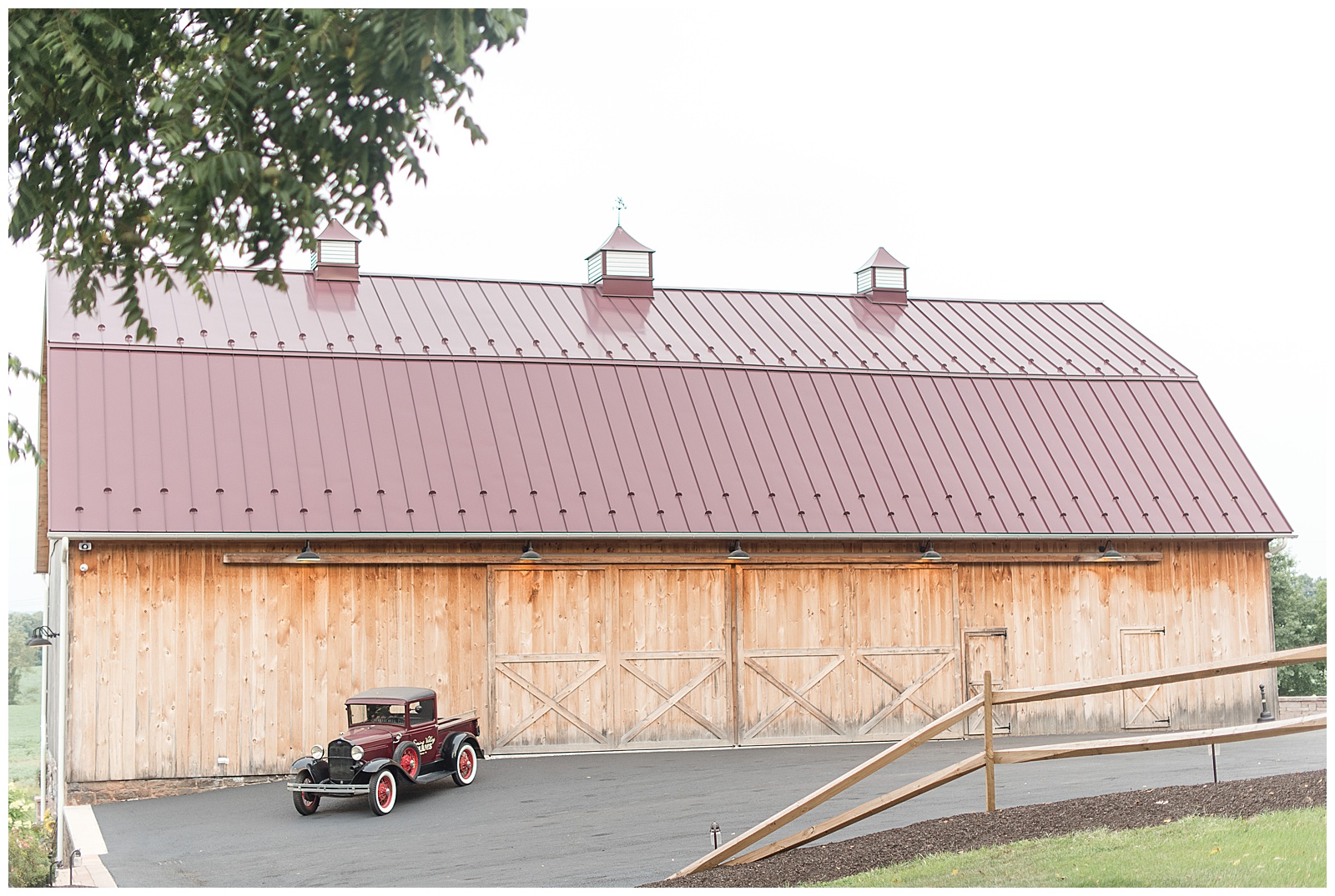 photo of maroon Model A Ford parked on driveway in front of wooden barn with maroon metal roof and car is on the left side of photo and wooden split-rail fence is on right side of photo at Spring Valley Farms in Dover, PA
