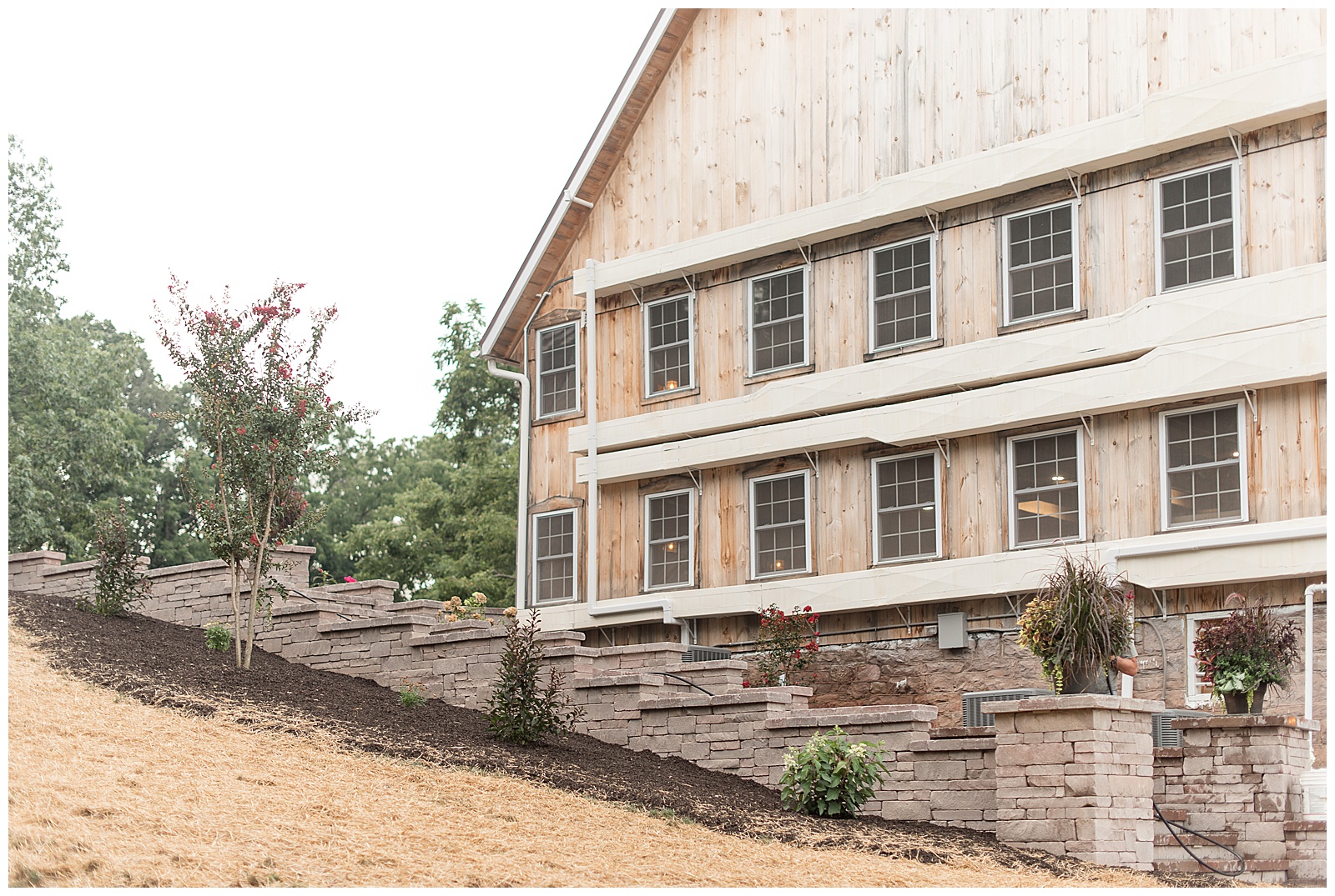 close up photo of exterior of barn on side with many windows and nicely landscaped stone wall with mulched and manicured flowerbeds at Spring Valley Farms in Dover, PA