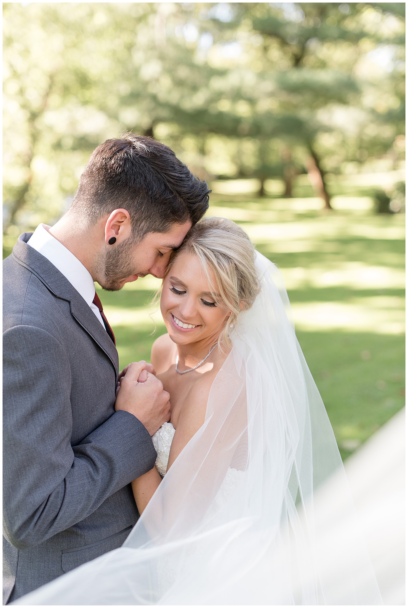 close up photo of couple smiling facing each other with groom on the left and bride on the right and they are facing each other holding hands resting their heads together with grass and trees and sunshine behind them at Riverdale Manor in Lancaster, PA