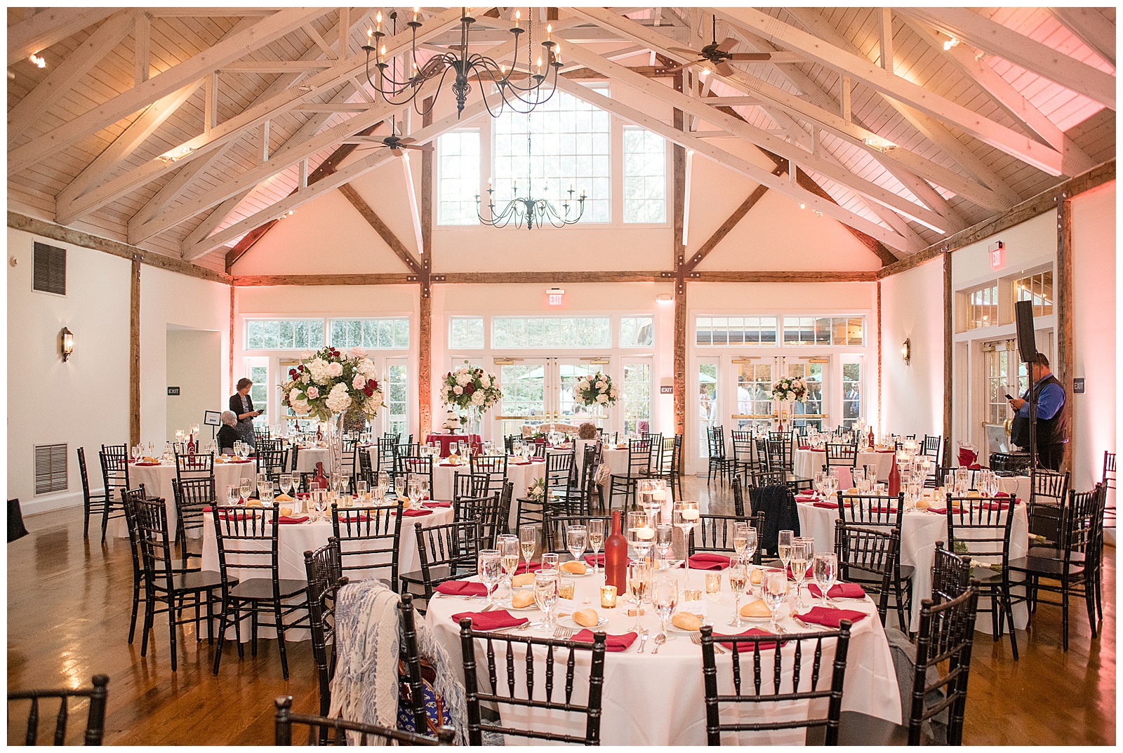 photo of the reception room held indoors in with white walls and exposed wooden and white beams with white linen covered tables and wooden chairs with red and white table settings and accents and there are no people in the room at Riverdale Manor in Lancaster, PA