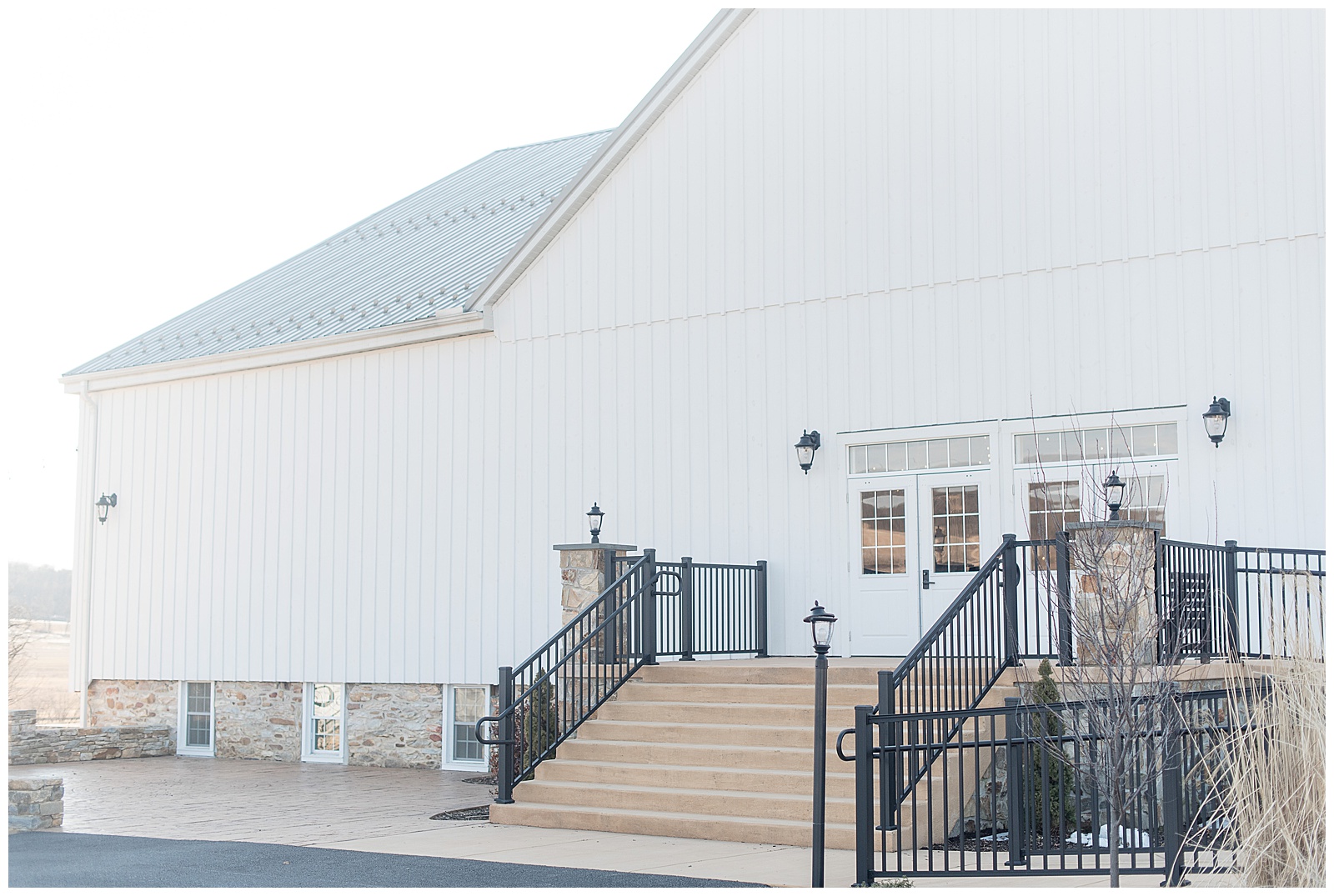 exterior photo of main entrance to large white barn with staircase leading up to white front doors and black wrought iron fence along staircase and sidewalk with black lamp post at bottom right of staircase at The Barn at Stoneybrooke in Atglen, PA