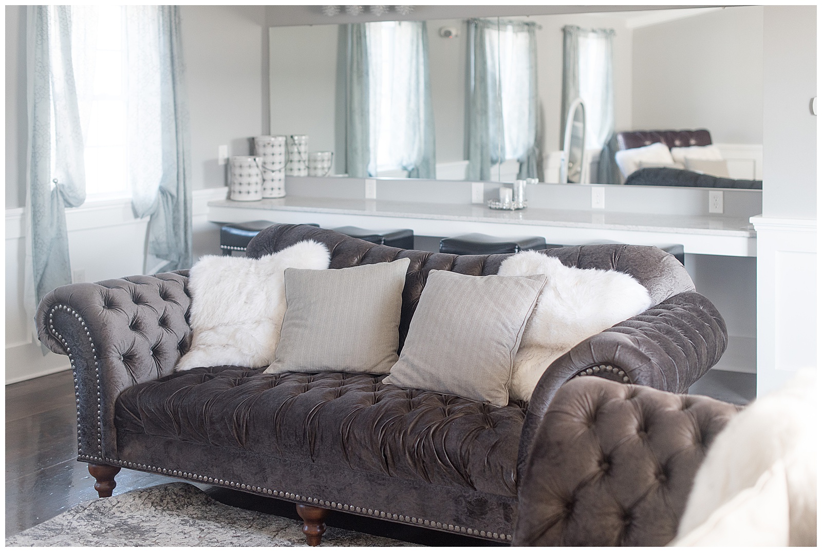 close up photo of large dark brown leather couch with gray and white pillows on it and countertop with mirror and stools and large white window behind it at The Barn at Stoneybrooke in Atglen, PA