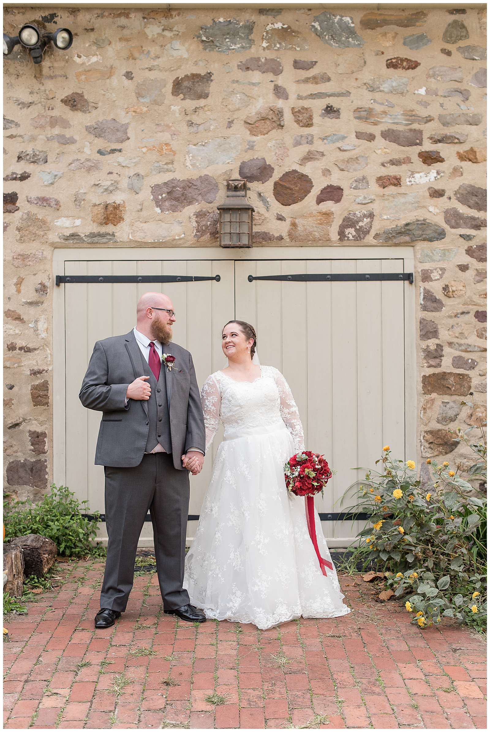 groom and bride smiling in front of stone building at historic poole forge