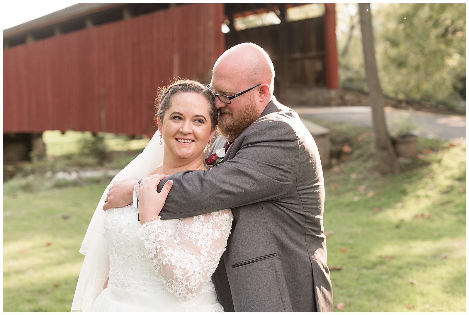 groom hugs bride in front of maroon covered bridge at historic poole forge