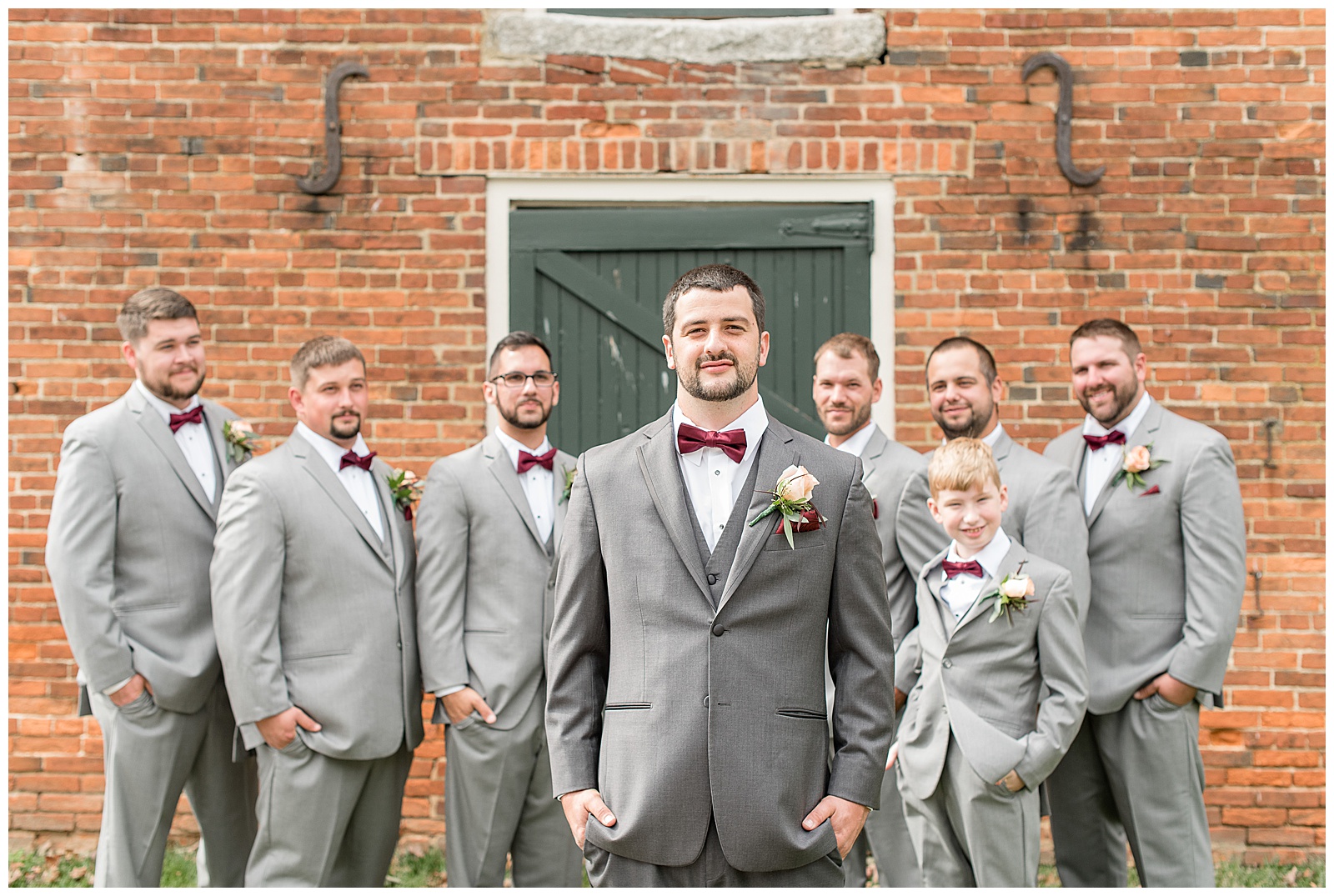 groom and groomsmen with hands in pockets by brick building at hayfields country club