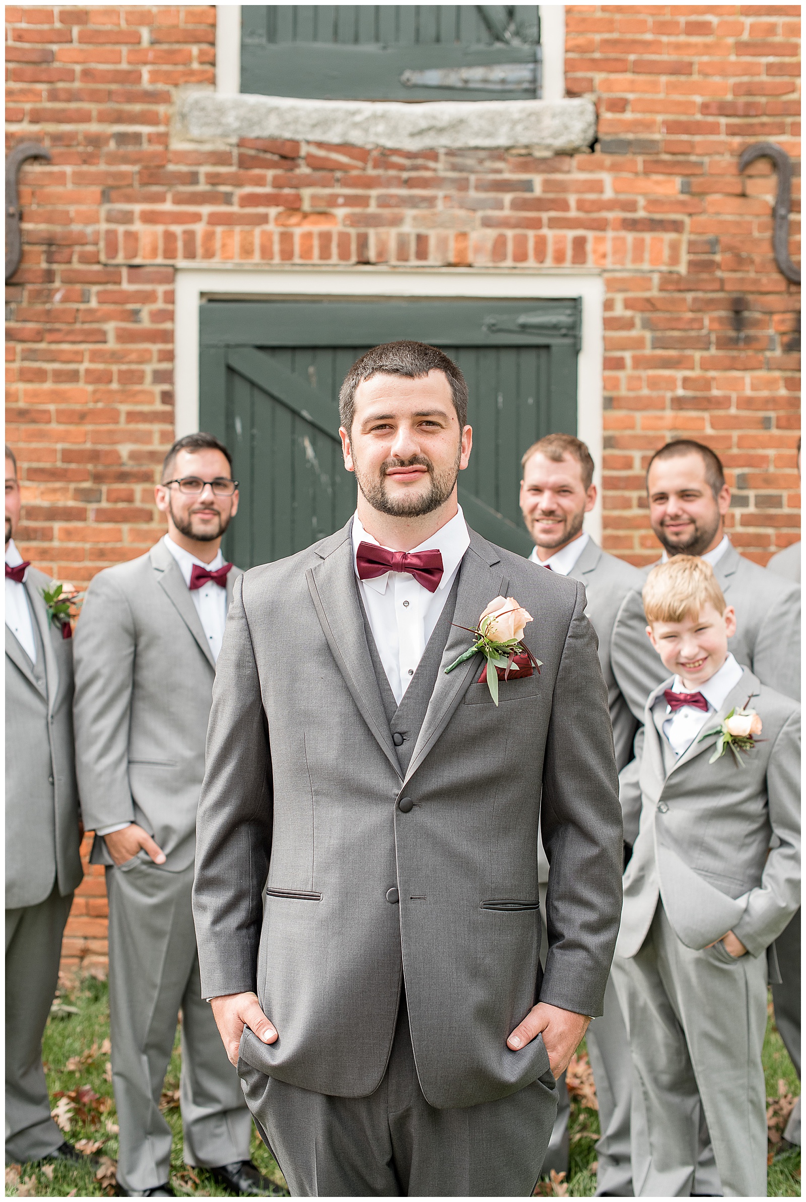 groom surrounded by groomsmen in gray suits by brick building at hayfields country club