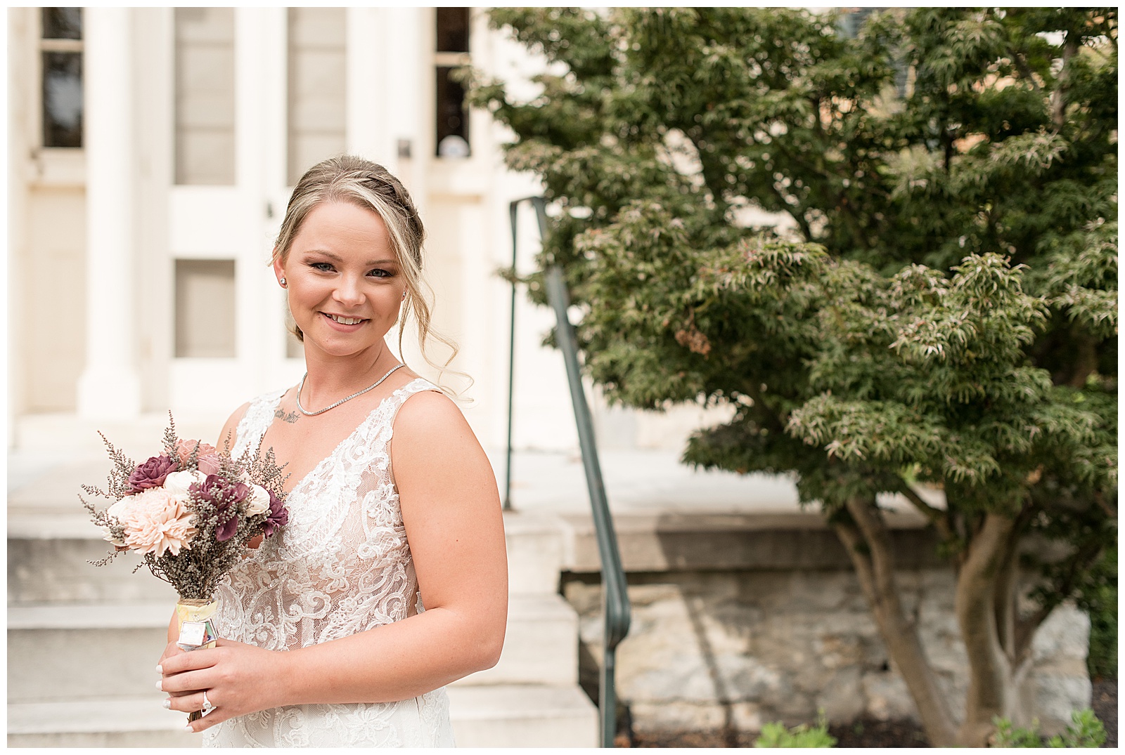 bride holding bouquet and smiling by stone building at hayfields country club