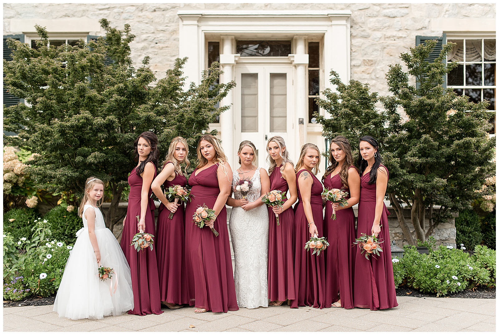 bride surrounded by bridesmaids and flowergirl in front of stone building at hayfields country club