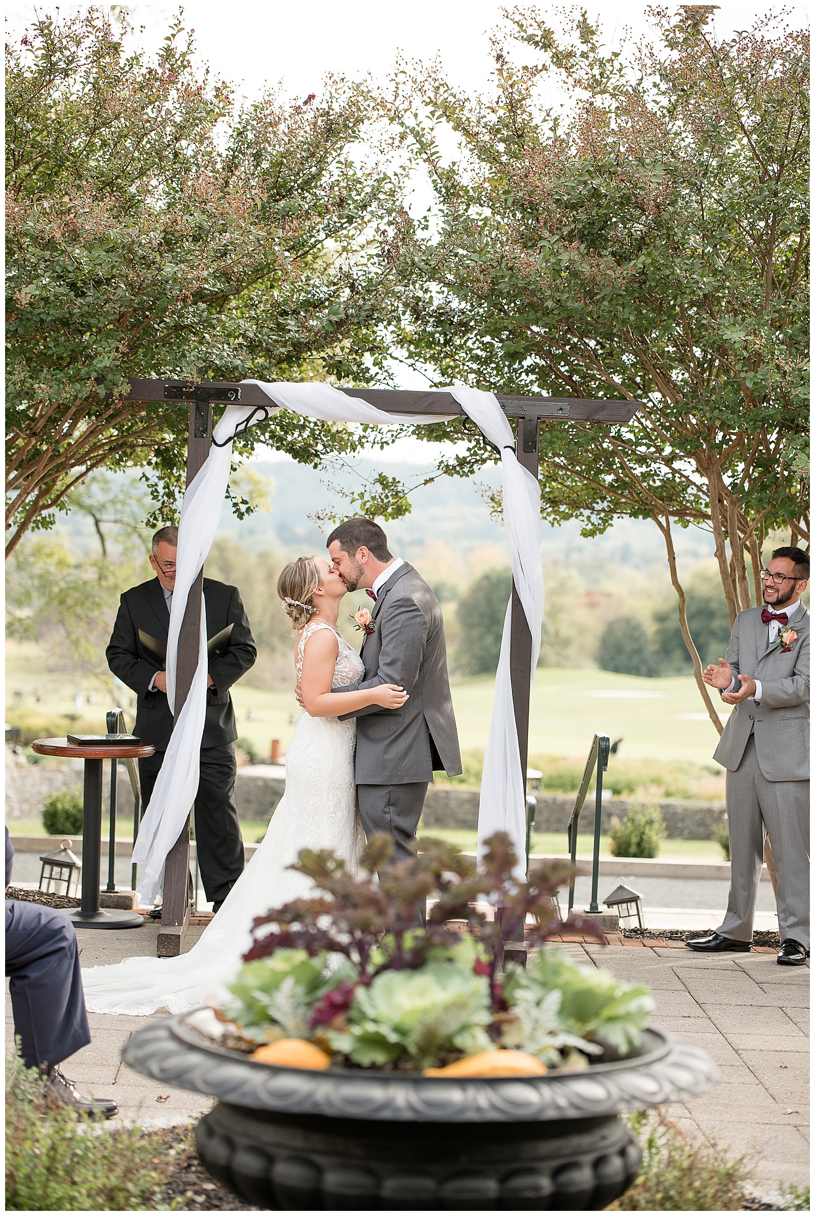 bride and groom kissing during wedding ceremony under wooden archway at hayfields country club