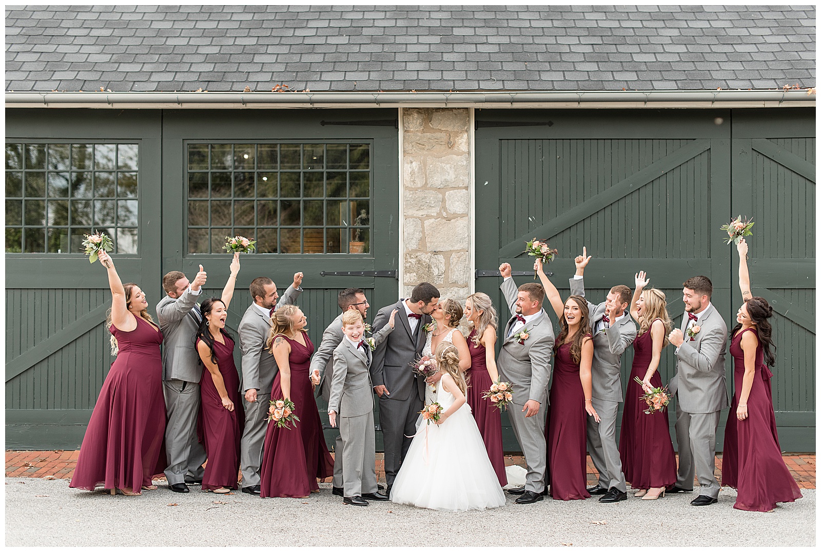 bridal party cheering as bride and groom kiss in front of building at hayfields country club