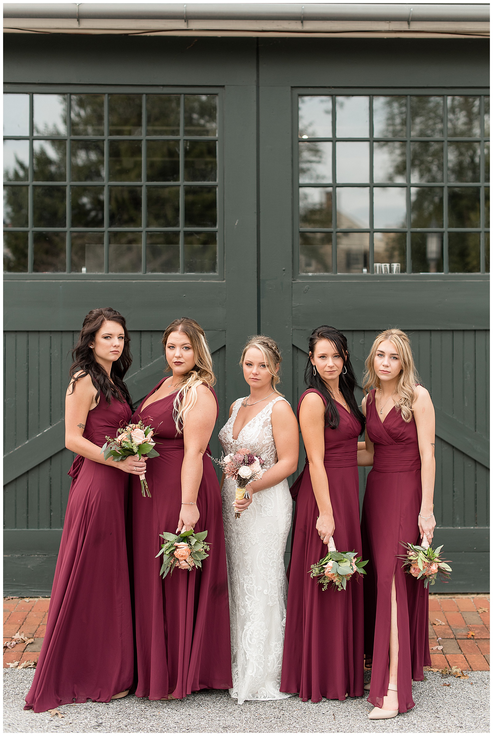 bride with bridesmaids in maroon dresses holding bouquets with large doors behind at hayfields country club