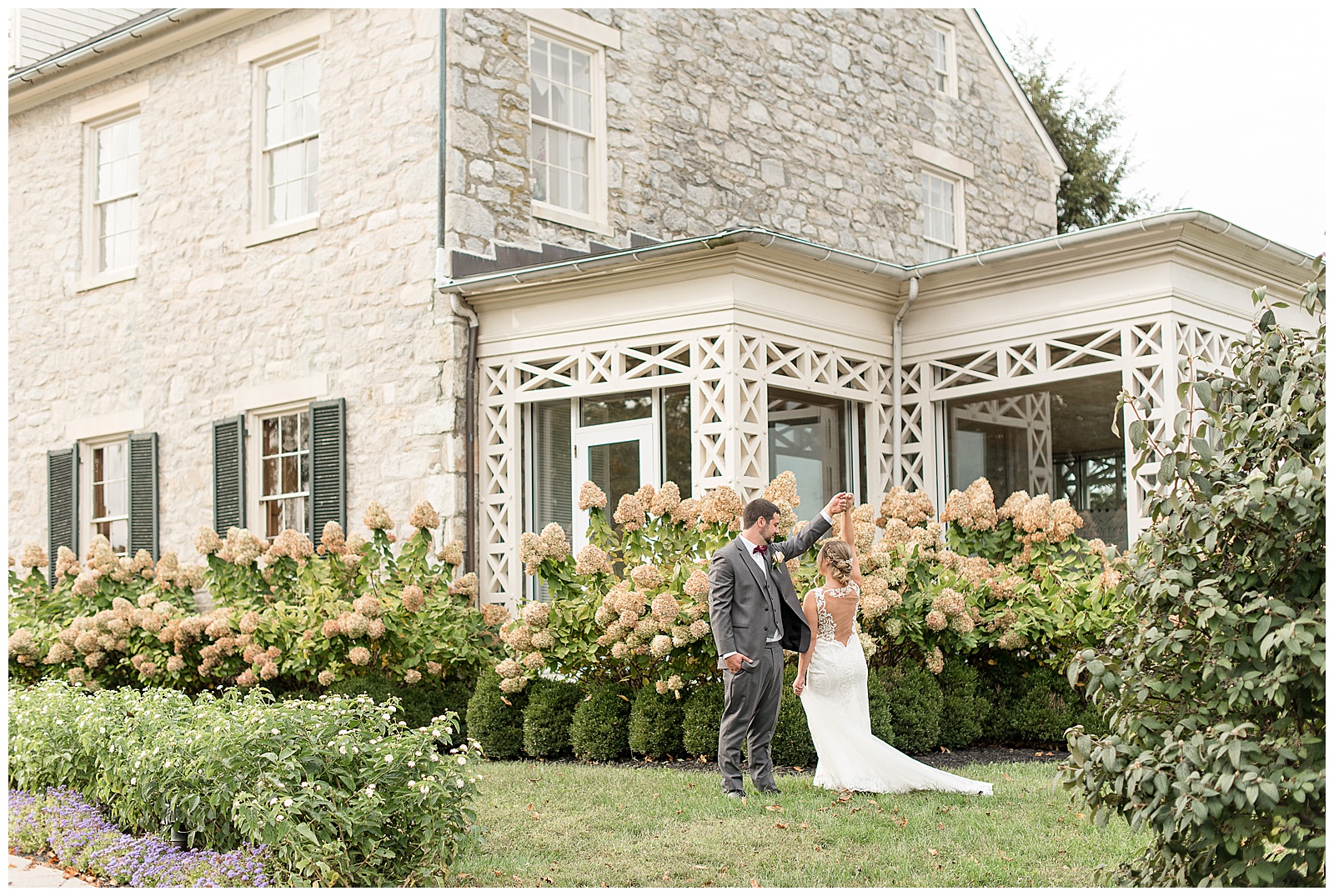 groom twirls bride in lawn beside beautiful stone building at hayfields country club