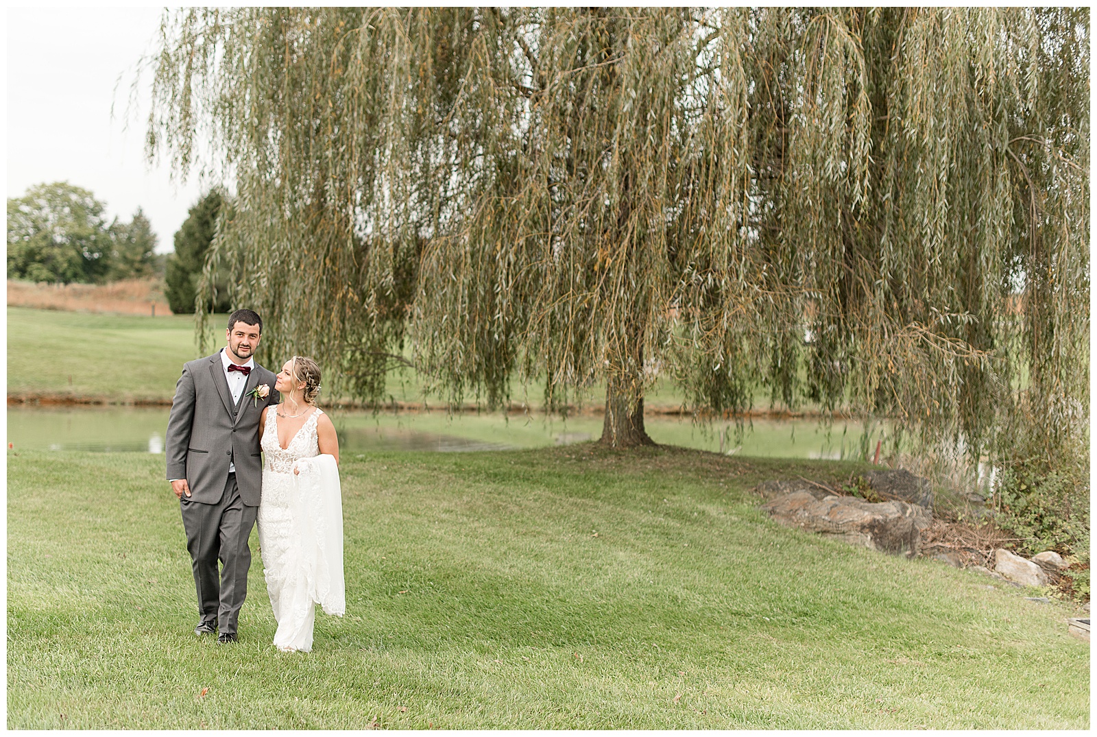 groom and bride walk toward camera with willow tree in background at hayfields country club