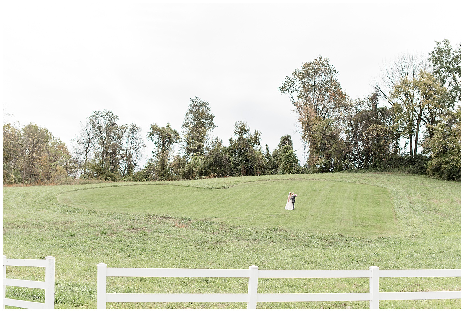 couple standing in large grass meadow with white fence on fall day at bluestone estate