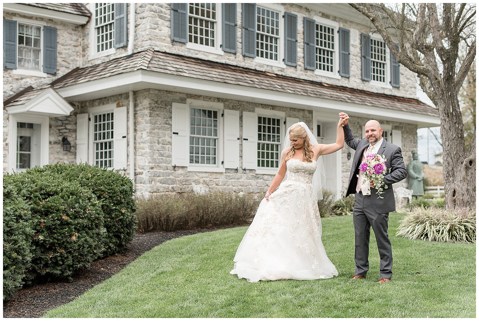 groom holds bouquet and twirls bride in front of historic stone house in lancaster pennsylvania