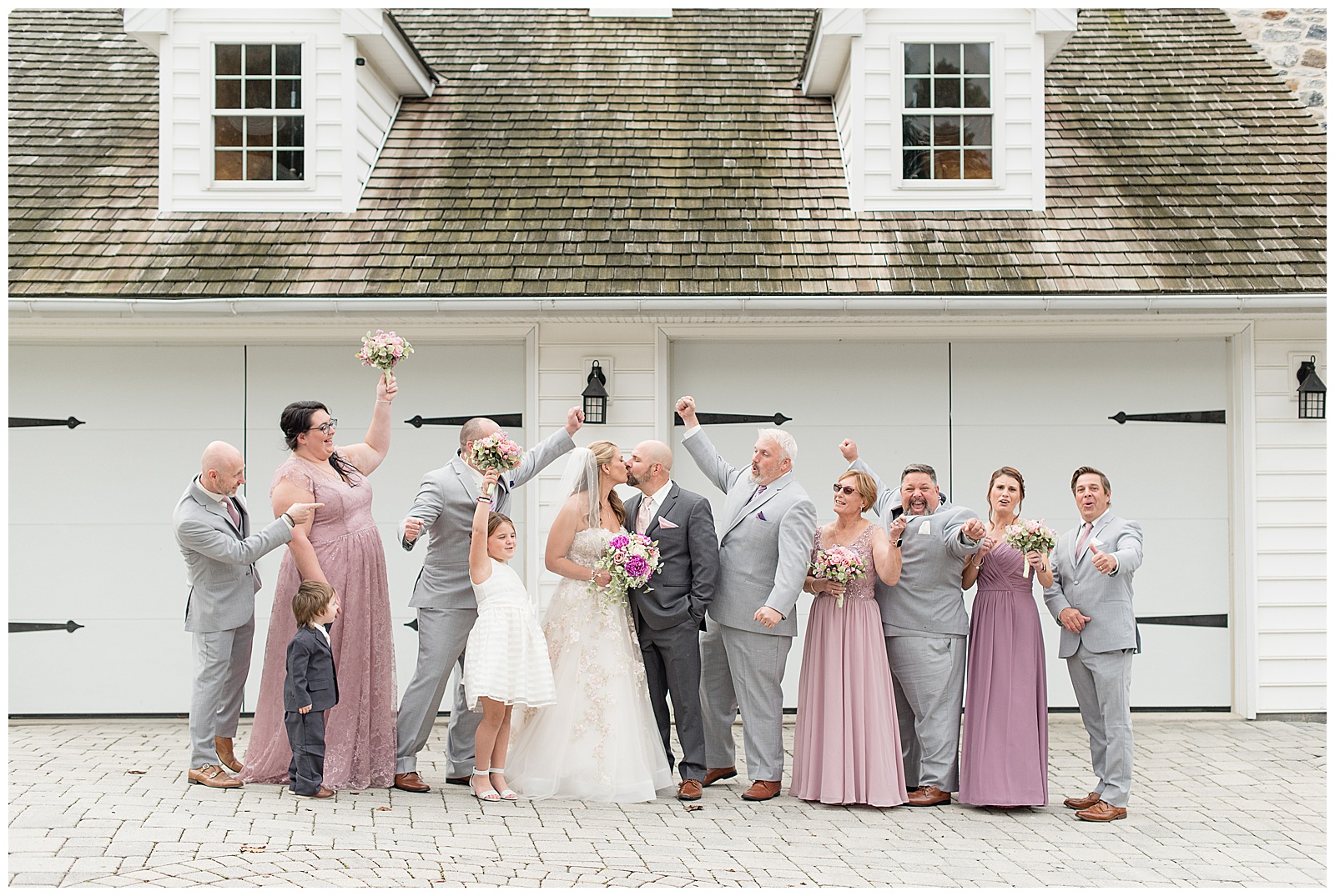 bridal party cheering for couple as they kiss by white barn at bluestone estate