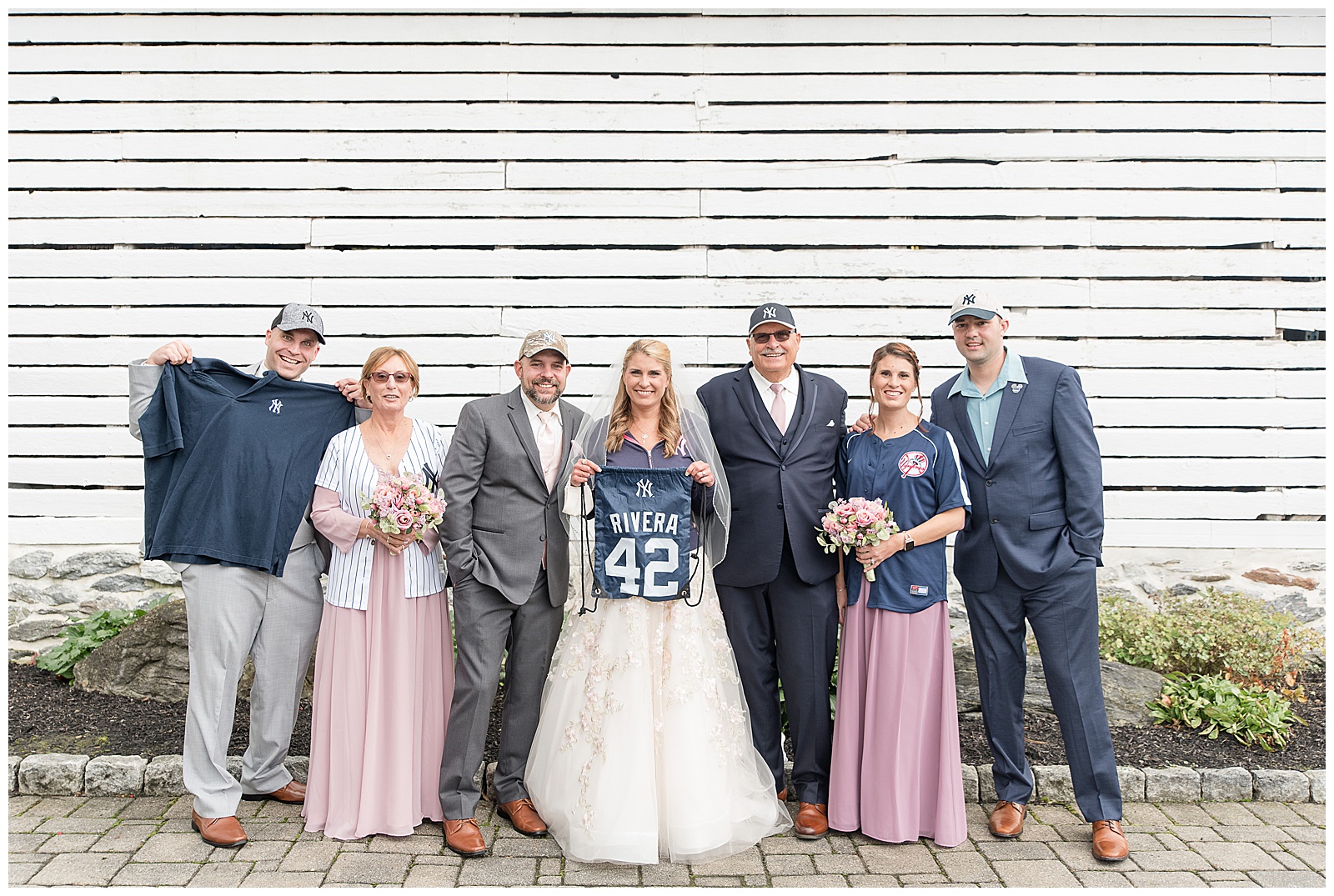 bride and groom with family displaying yankees baseball apparel by white wooden wall in lancaster pennsylvania