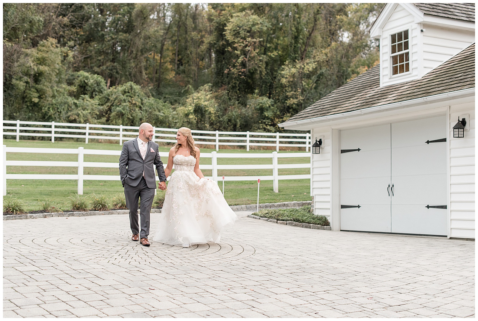 groom and bride holding hands walking on stone driveway by white fence and barn in lancaster pennsylvania