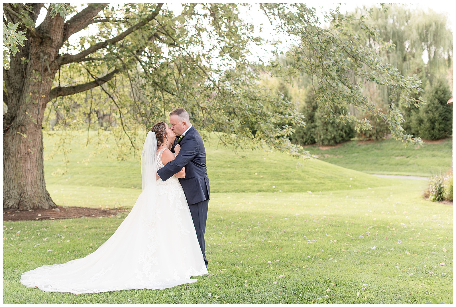 groom wrapping arms around bride as they share a kiss under large tree