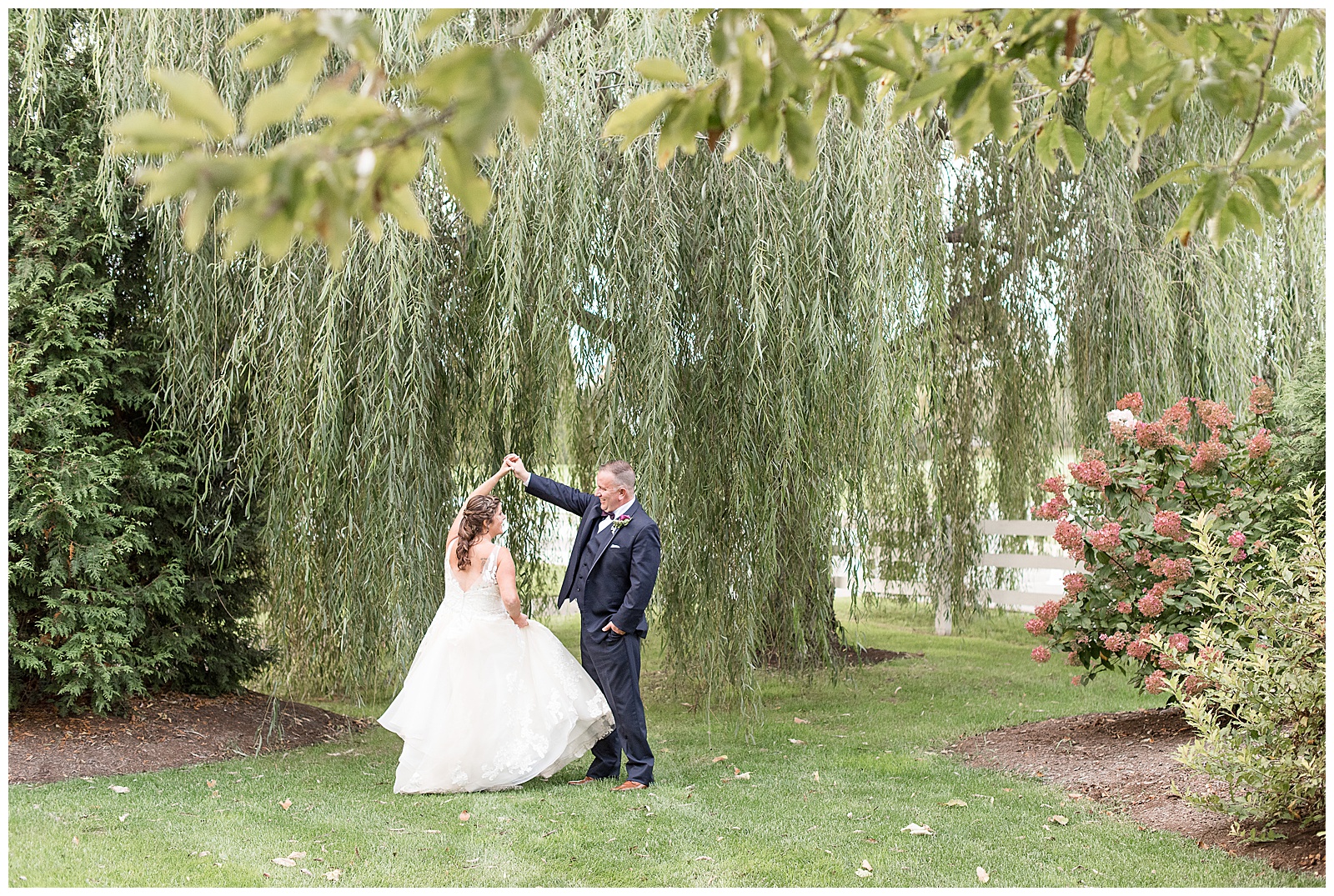 husband twirling wife in front of willow tree at Stoltzfus Homestead and Gardens