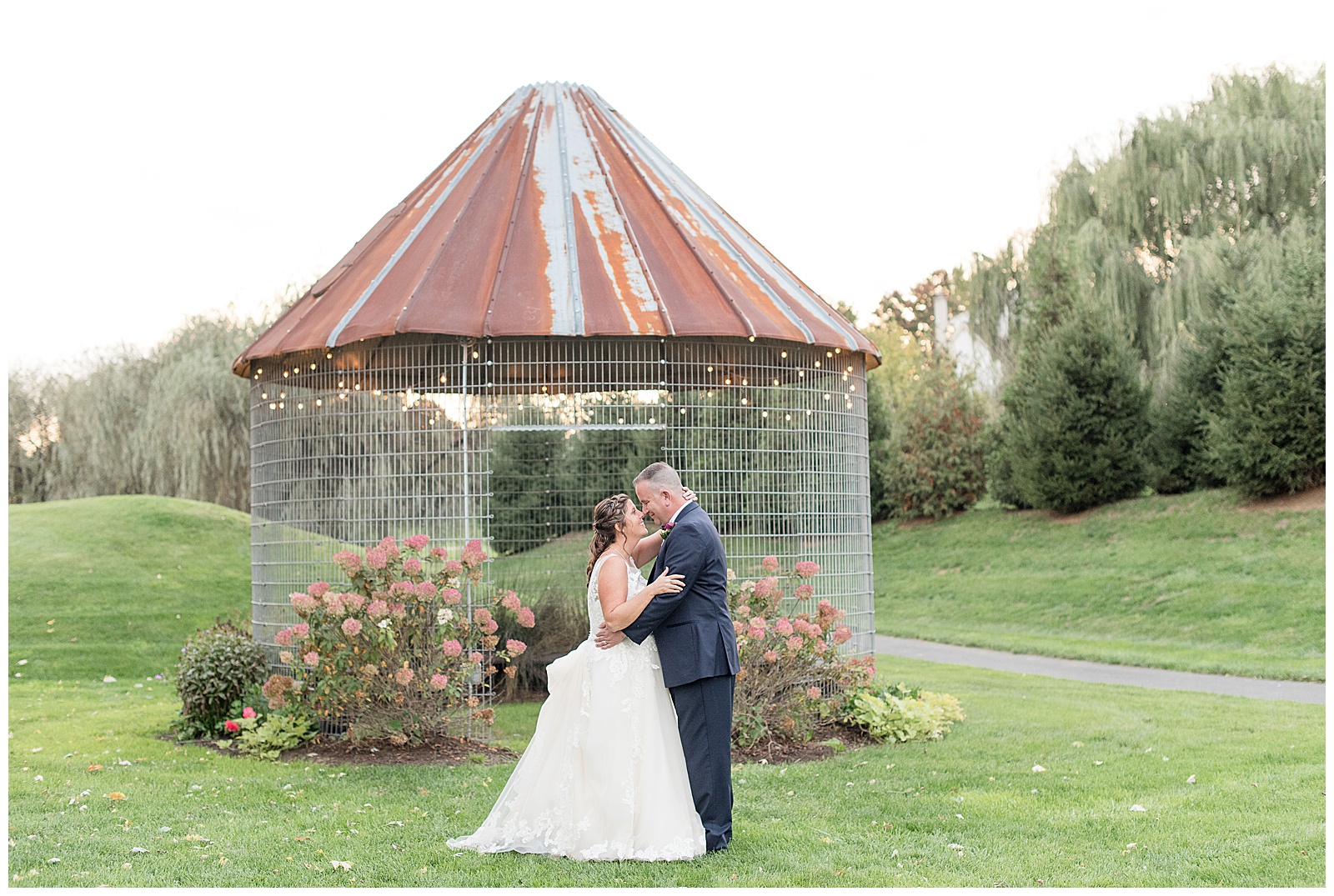 bride and groom facing each other with foreheads touching and corn crib behind during sunset photos 