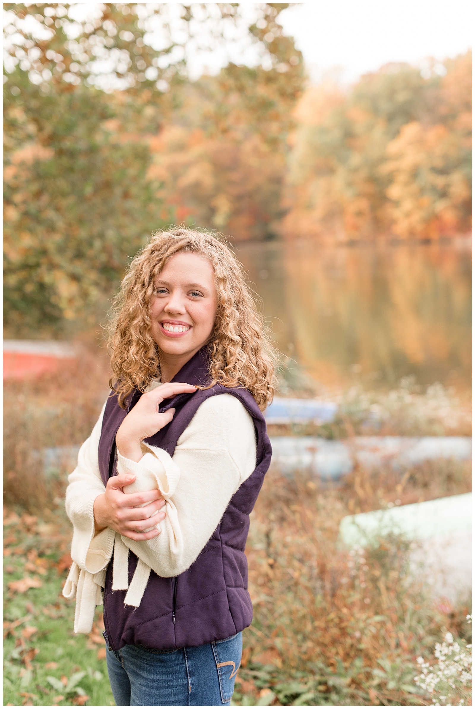 senior girl rests hands by shoulder in front of fall foliage at speedwell forge lake