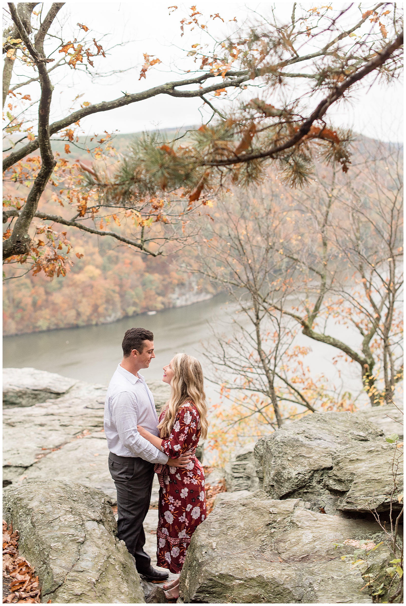 couple hugging smiling atop large rock lookout with fall foliage and river below in holtwood pennsylvania