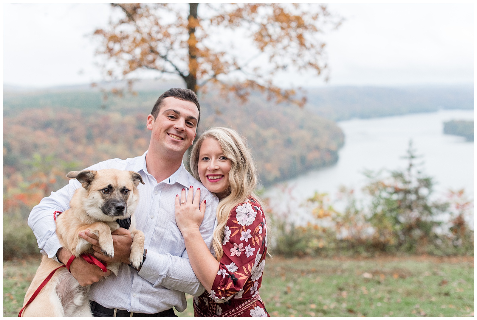 couple snuggles holding puppy at pinnacle point on cloudy colorful fall day in holtwood pennyslvania