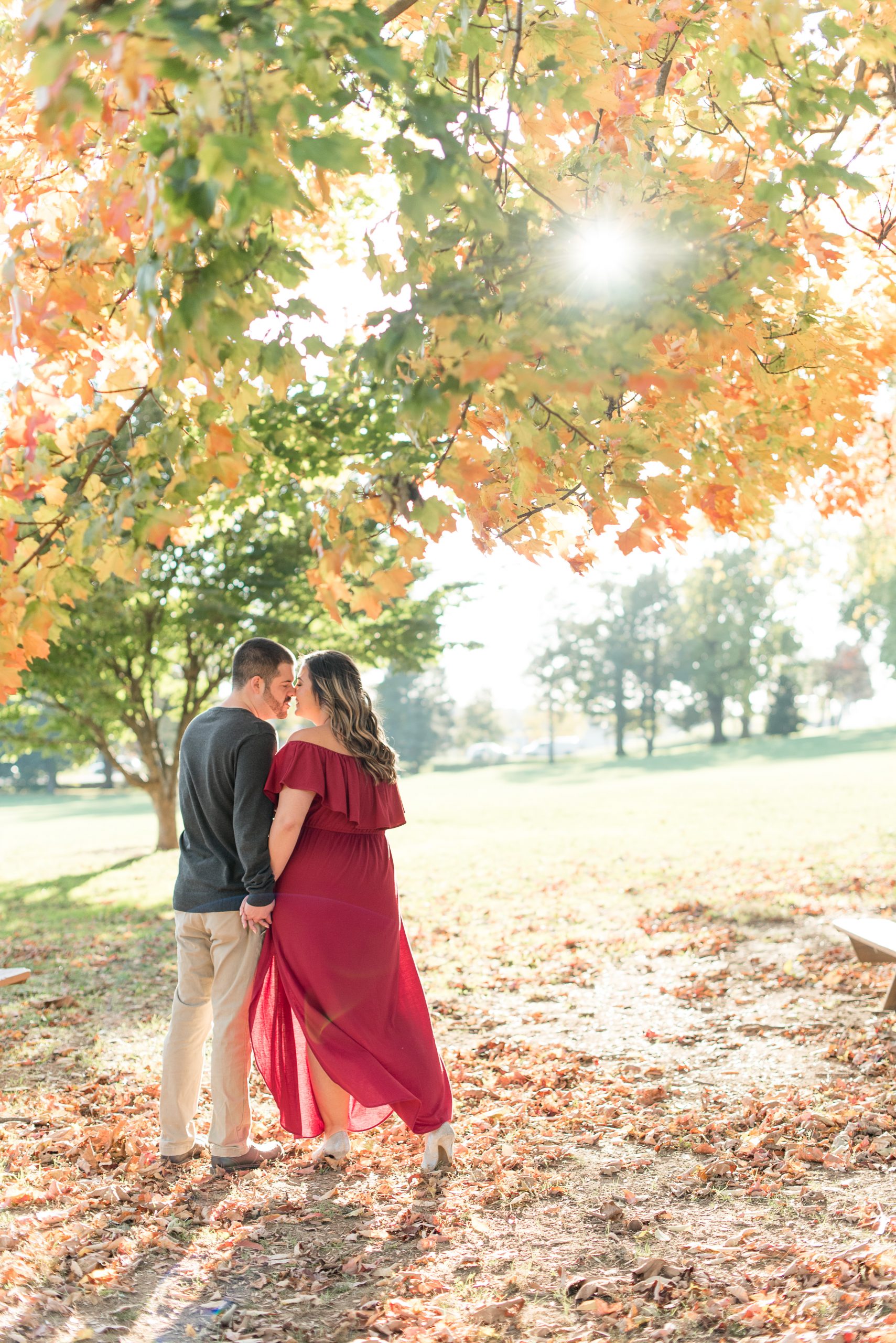 couple almost kissing under bright leaves of tree on fall evening at long's park