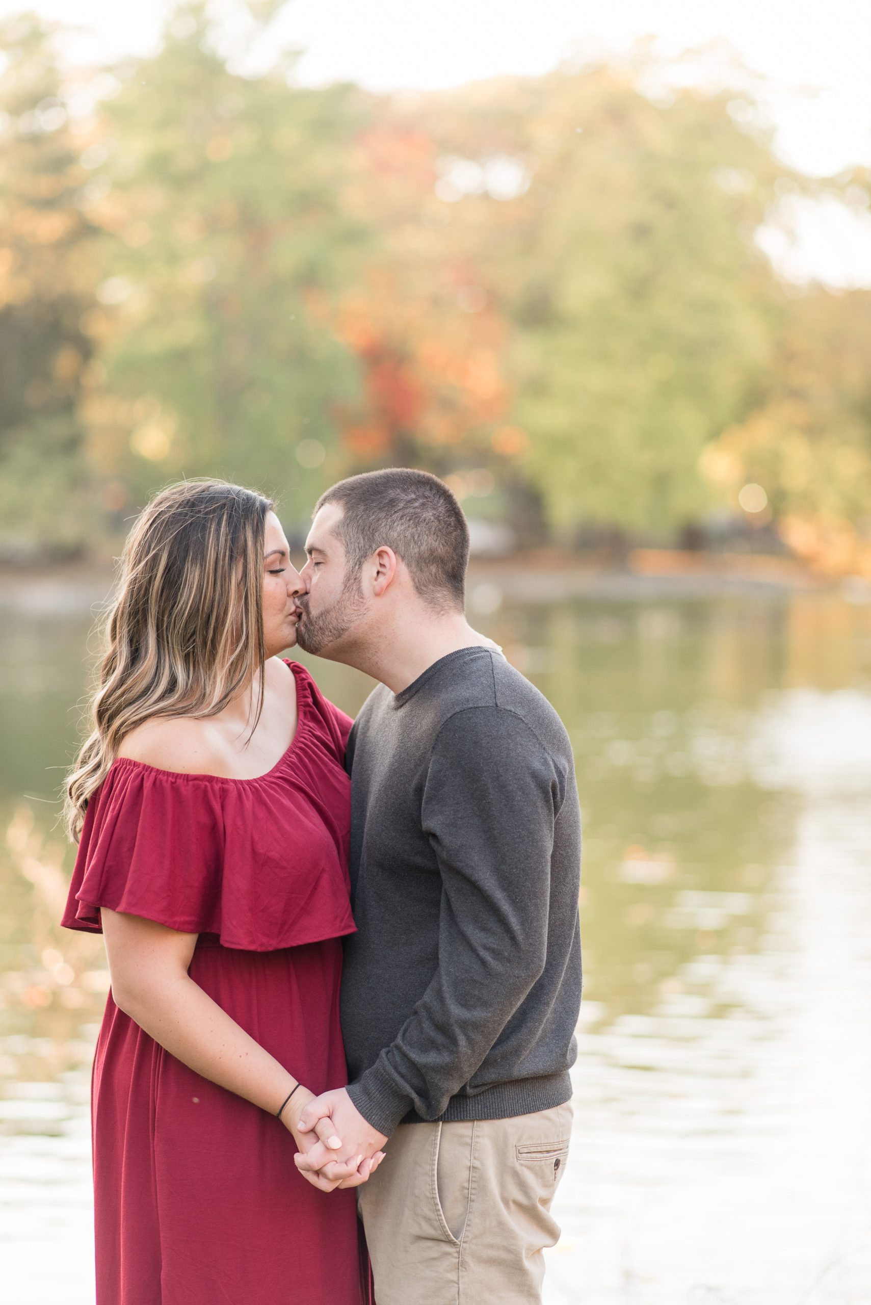couple kisses with pond and colorful leaves behind them at long's park