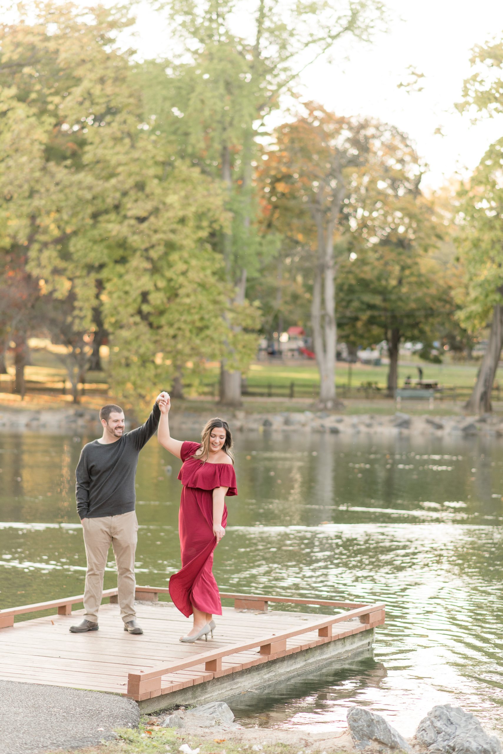 guy twirls girl on dock by pond at long's park on fall evening