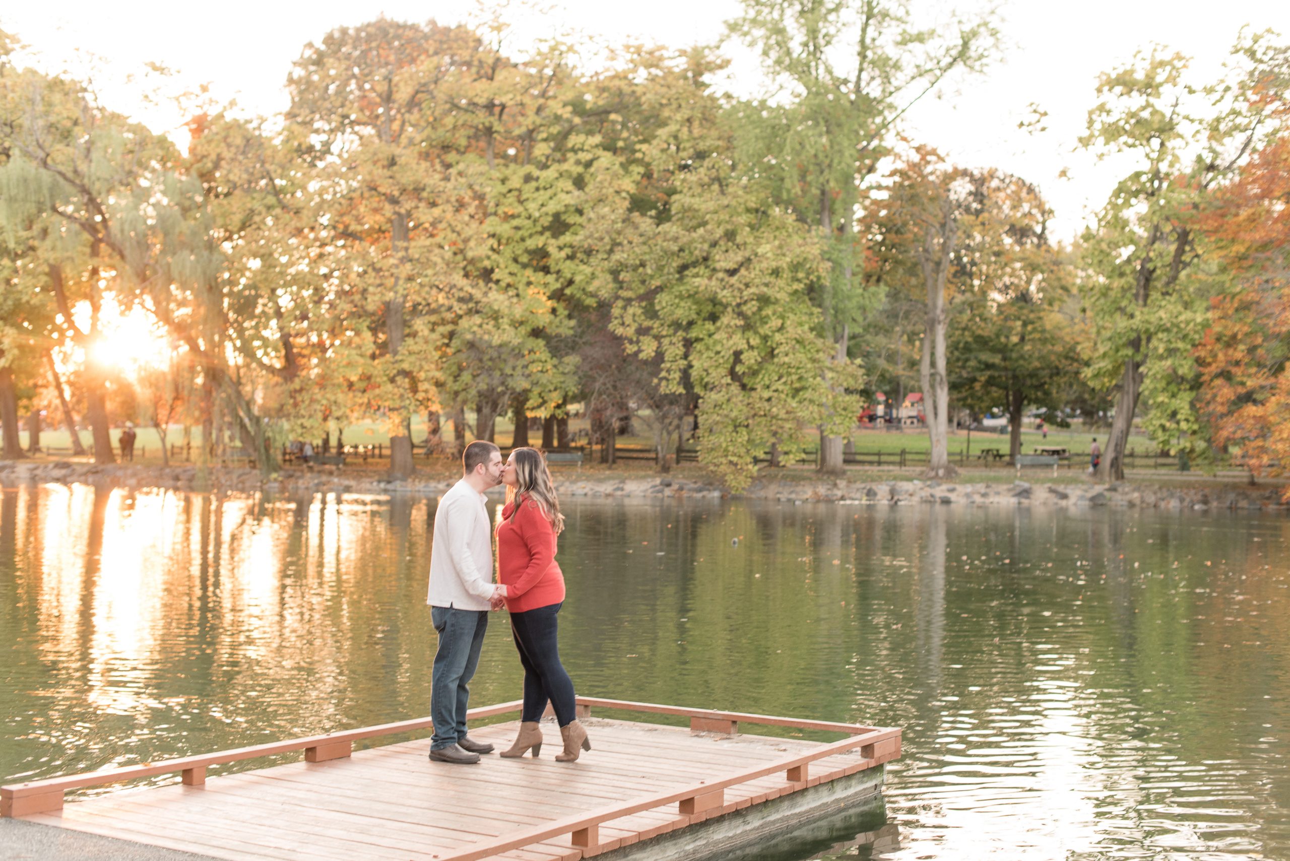 couple kissing on dock by pond with leaves changing colors behind them in lancaster pennsylvania