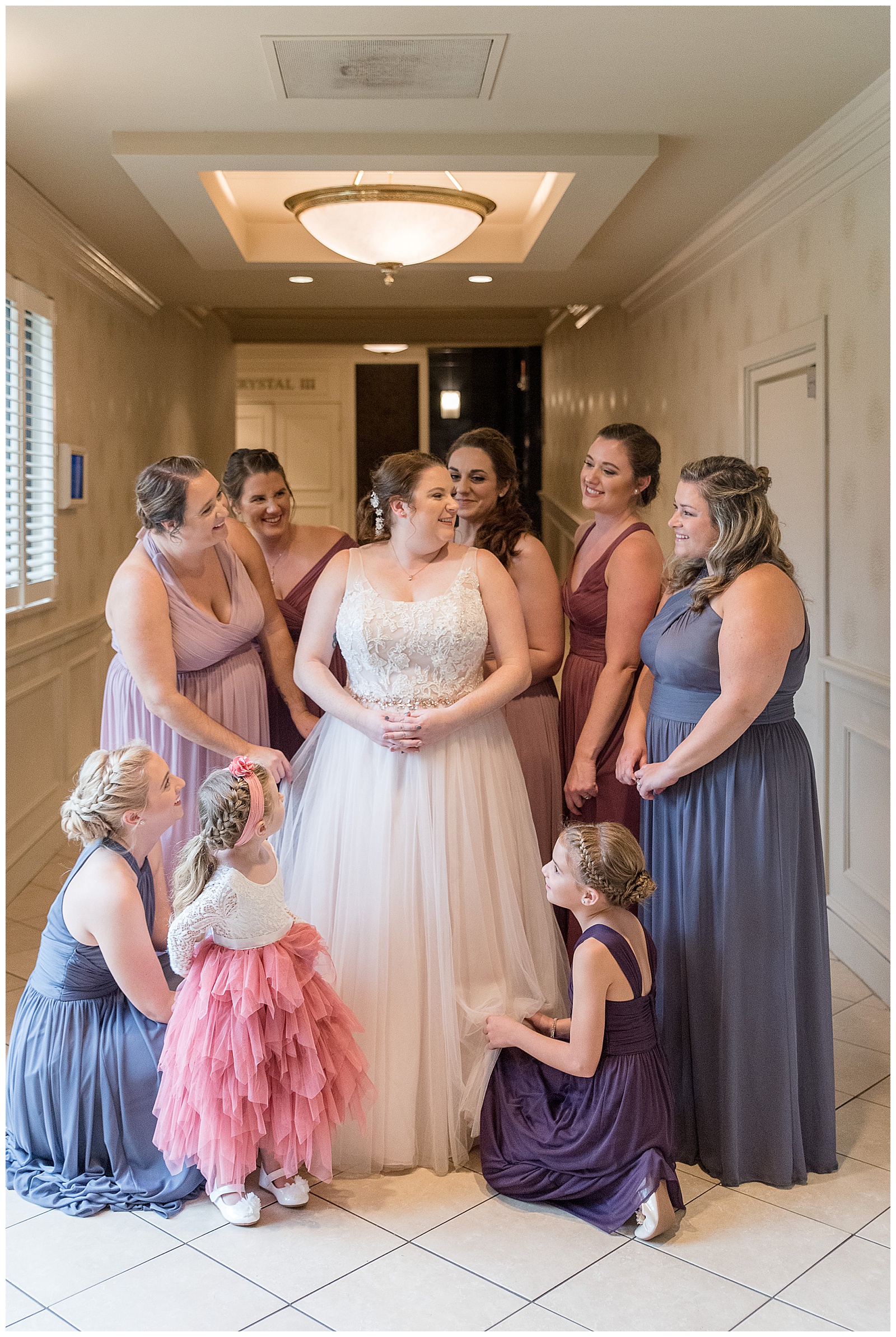 bride smiling surrounded by her bridesmaids and flower girl in beige hallway at eden resort