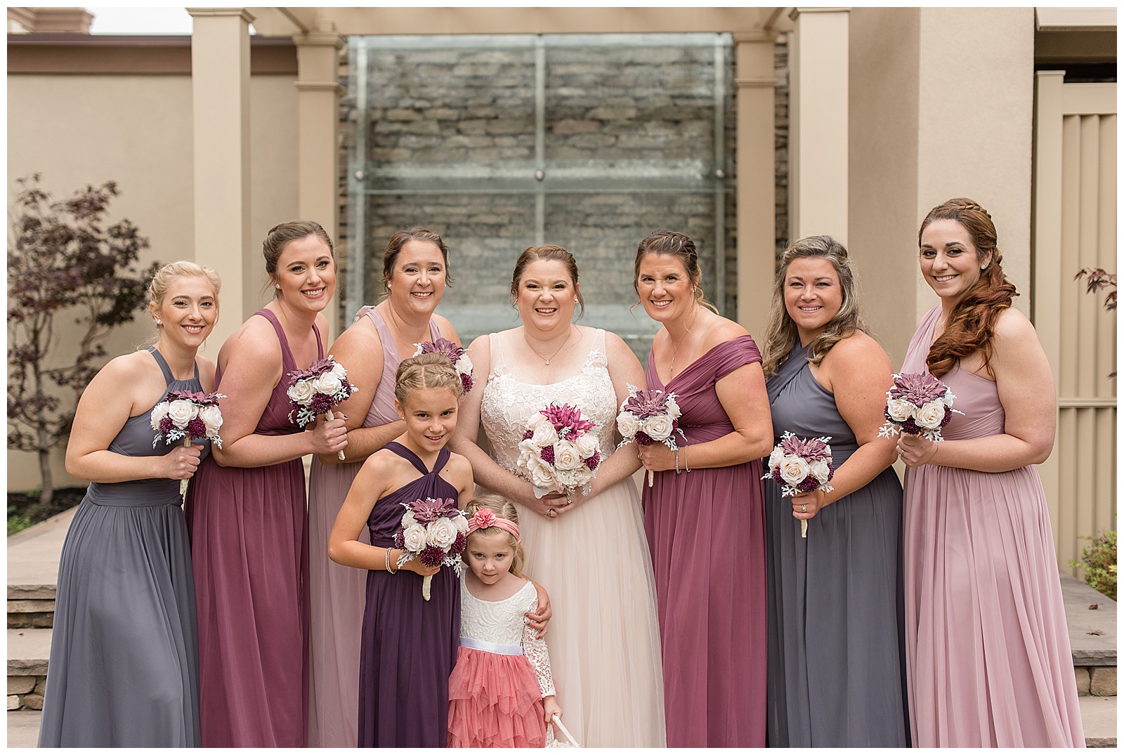 bride with her bridal party in shades of pink and purple dresses holding bouquets
