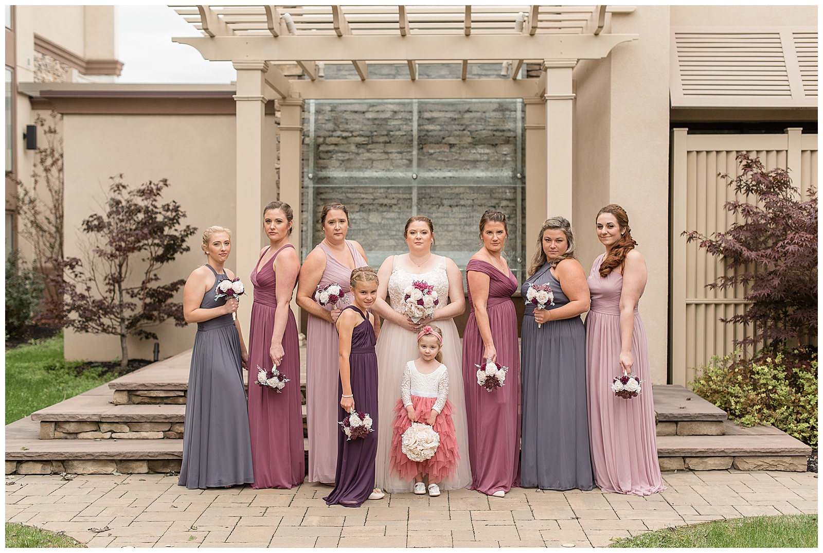 bride and bridesmaids in pink and purple dresses holding bouquets by wooden trellis at eden resort