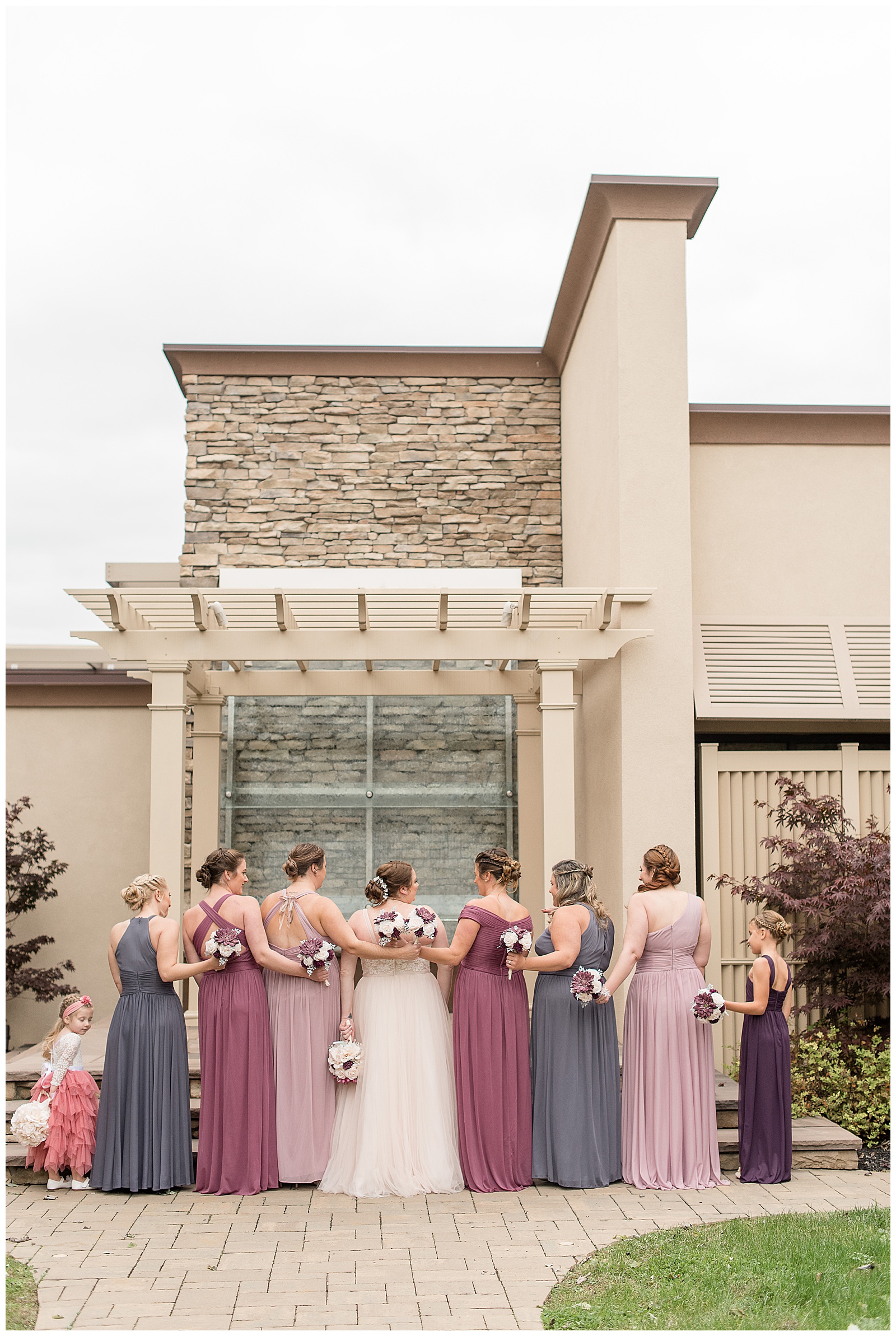 bride and bridesmaids with backs to camera and arms interlocked along pathway outside eden resort