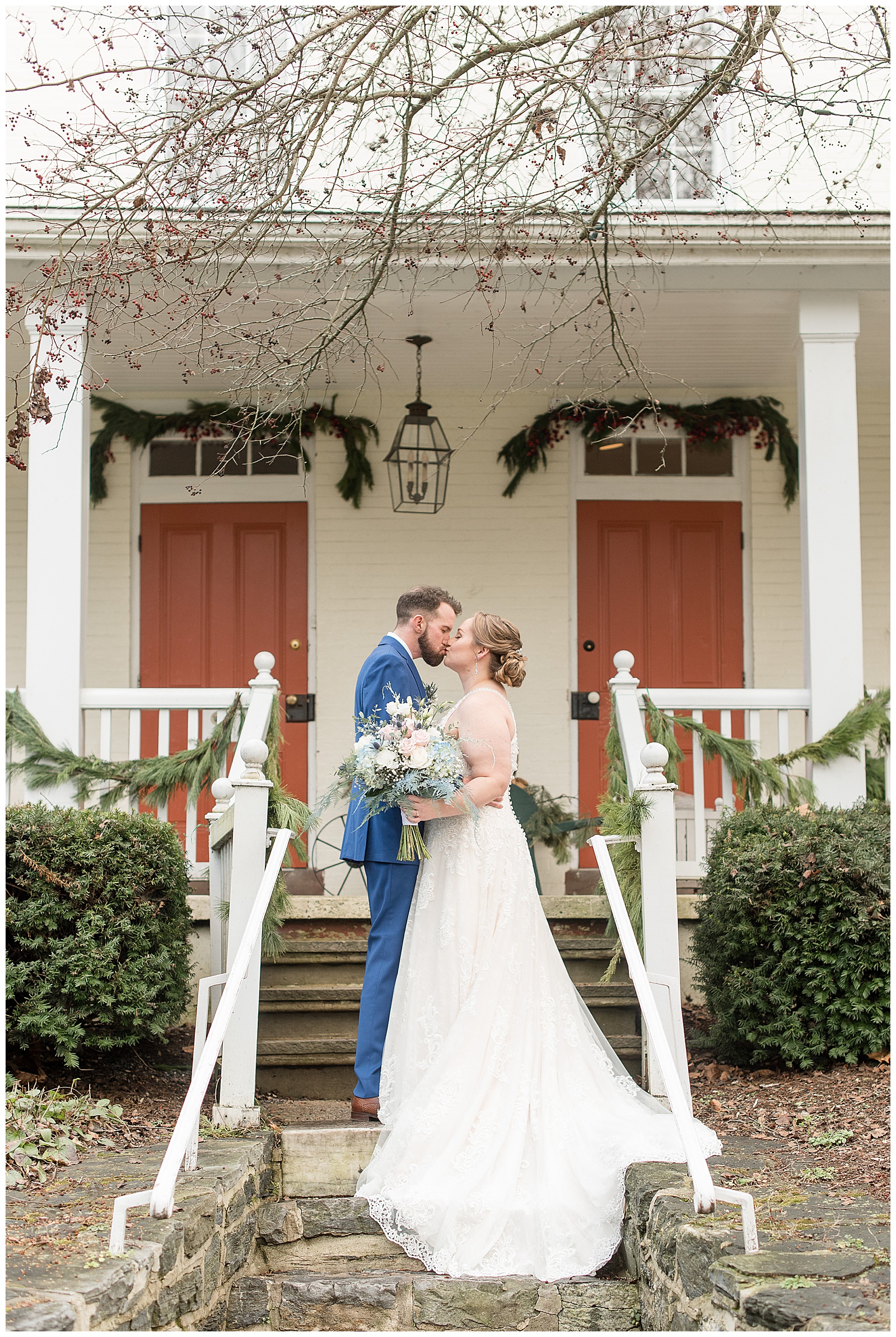bride and groom kissing on steps of white home decorated with garland at riverdale manor