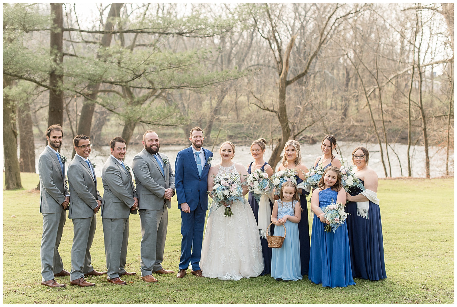 bridal party along river in grass yard on sunny winter day at riverdale manor
