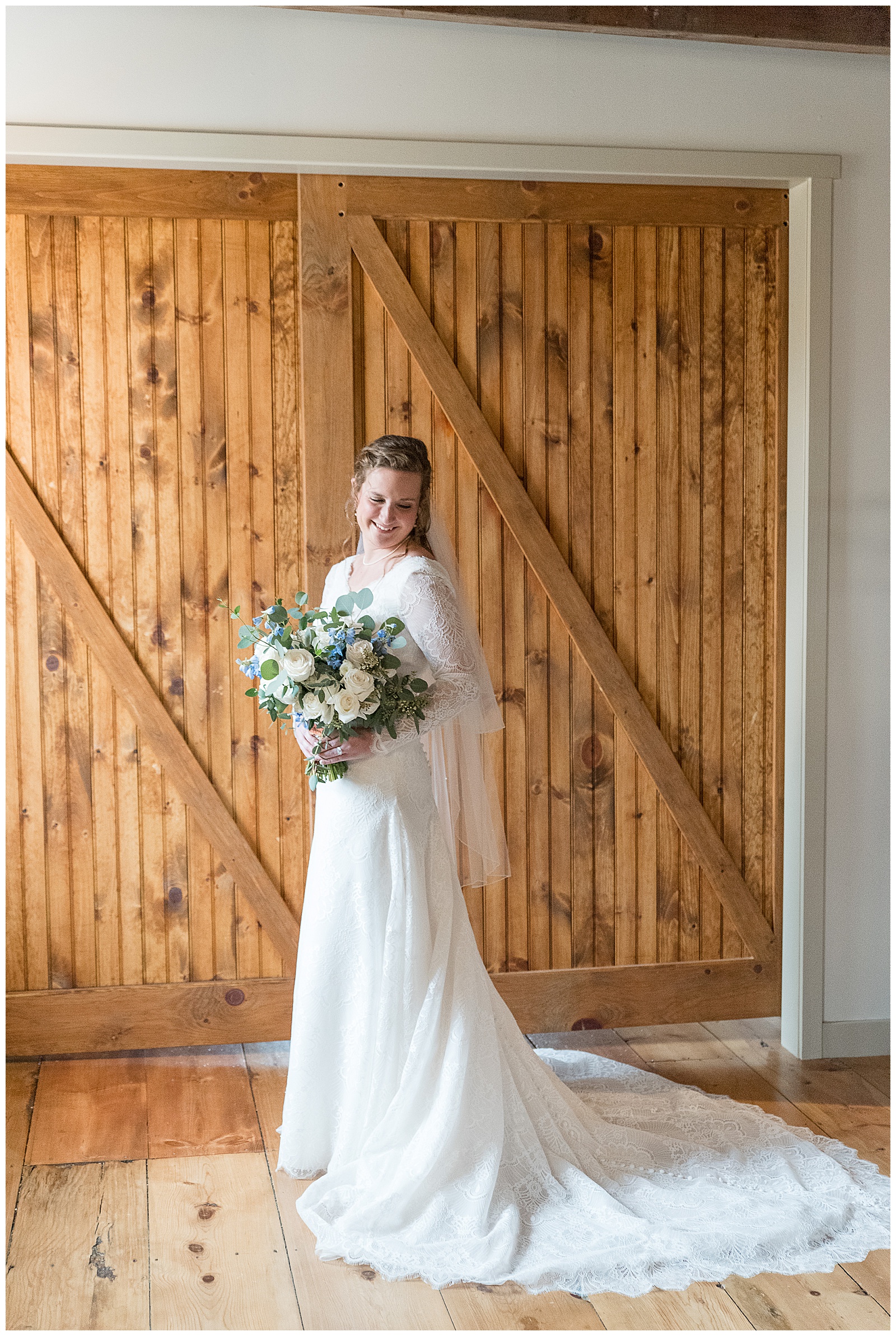 bride holding beautiful bouquet in front of large rustic wooden barn door smiling at the mill at manor falls