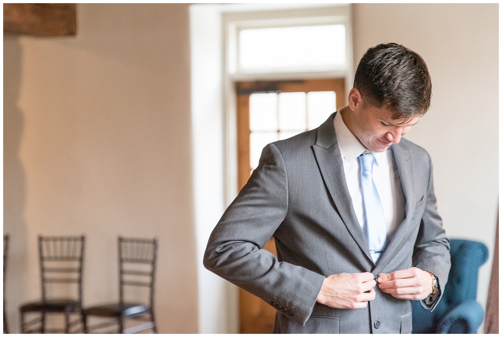 groom getting ready and buttoning light gray suit at the mill at manor falls