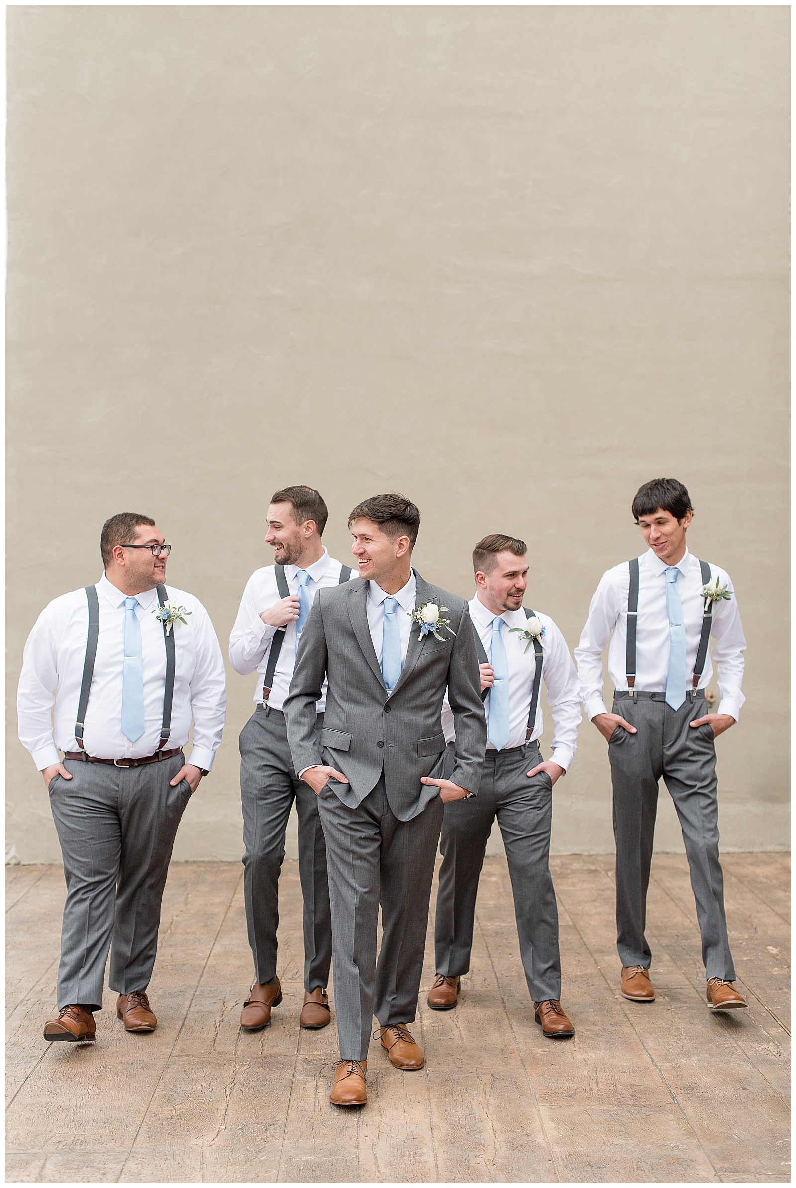 groomsmen wearing gray pants with suspenders and light blue ties with white shirts with groom
