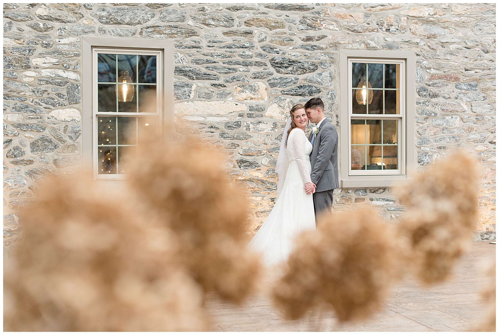 bride and groom cuddling by beautiful gray stone wall of barn at the mill at manor falls