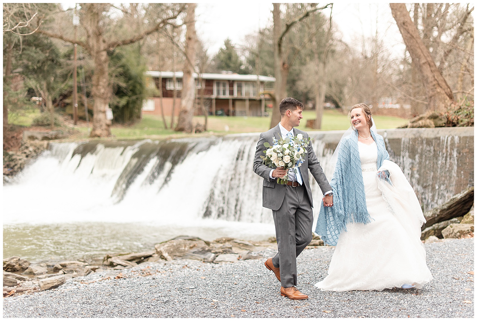 couple walking away from waterfalls holding hands as groom also holds bride's bouquet in lancaster pennsylvania