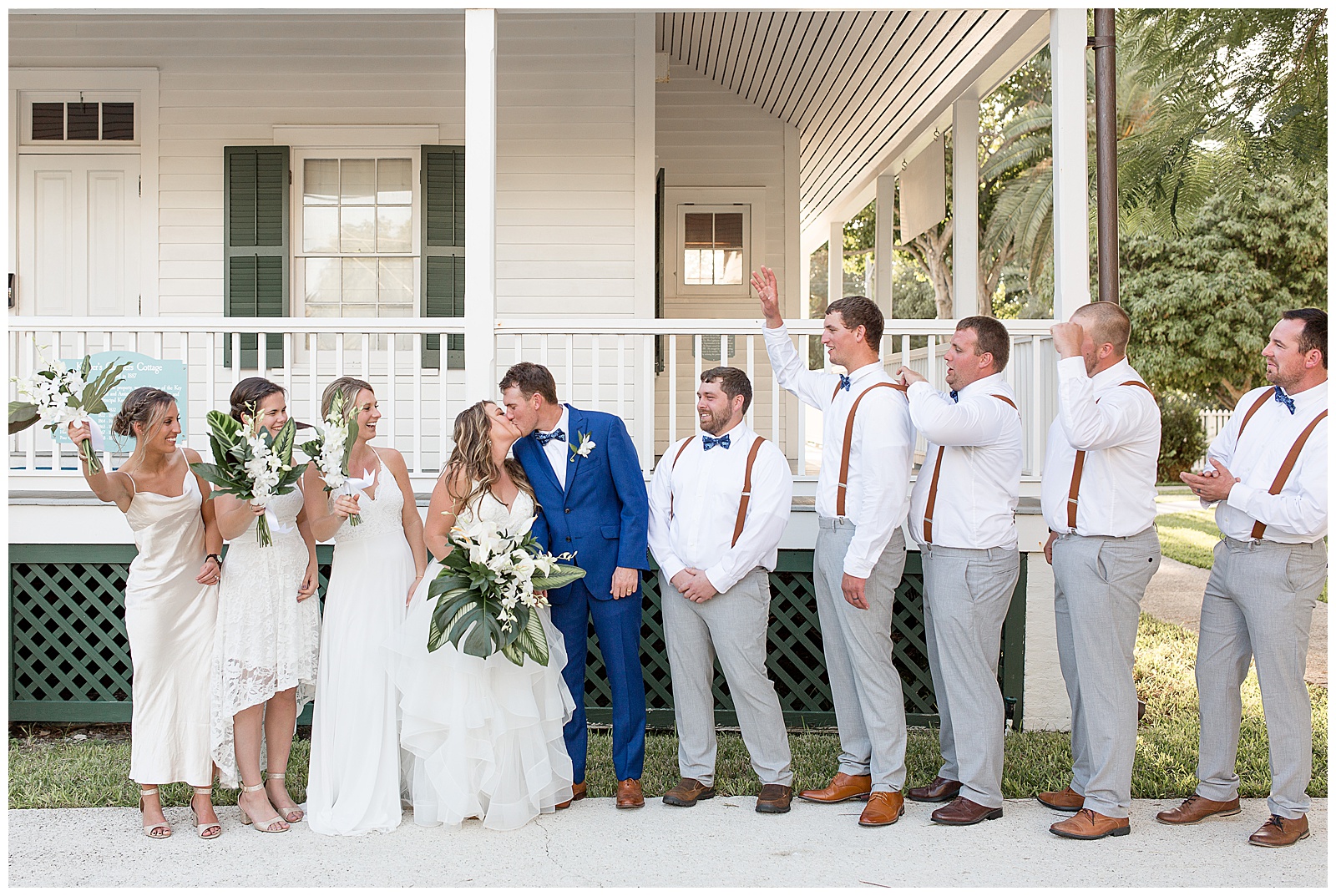 bride and groom kissing surrounded by bridal party who is cheering them on outside white cottage at hemingway house