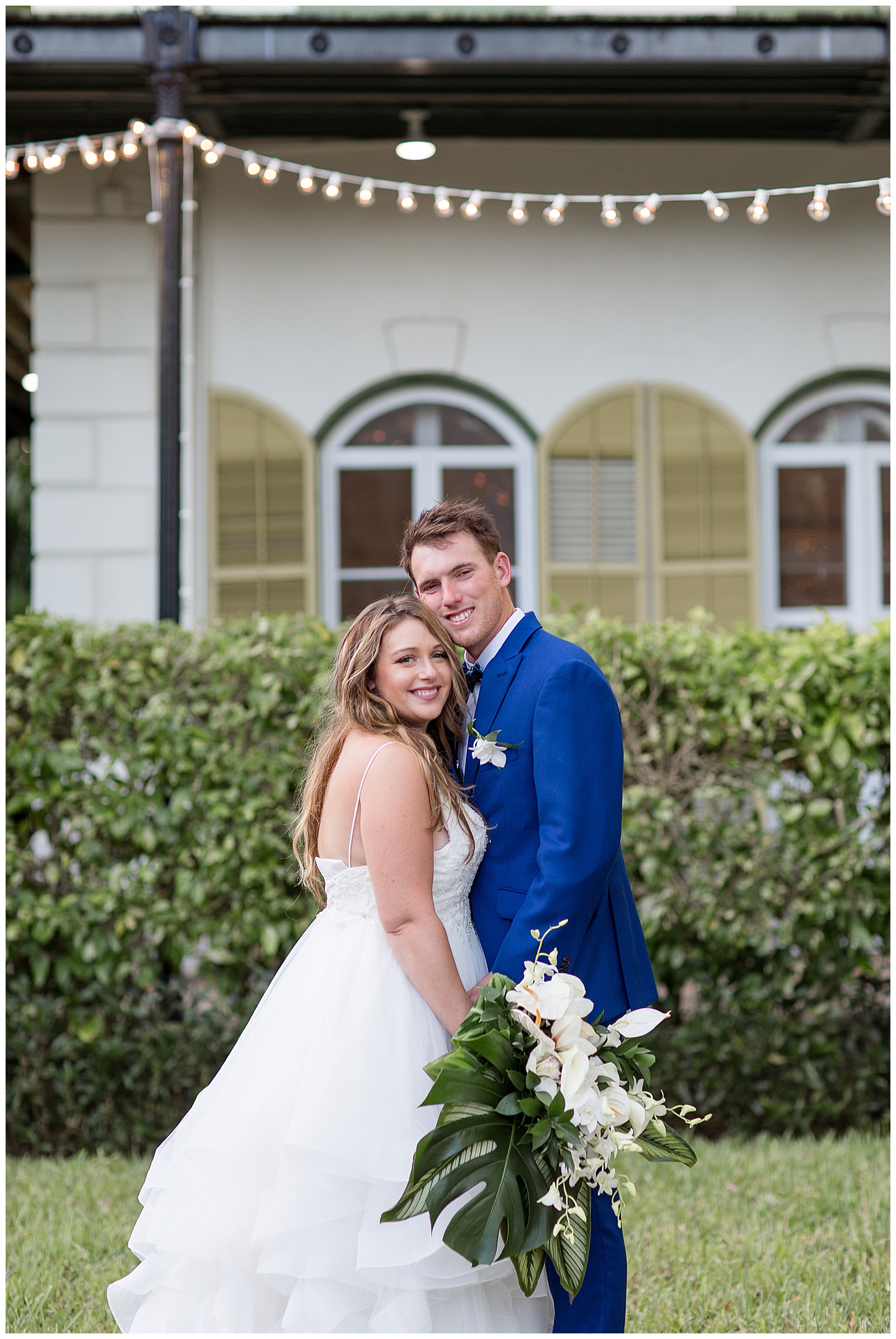 bride and groom hugging on lawn by hedge row and smiling as bride holds bouquet at hemingway house
