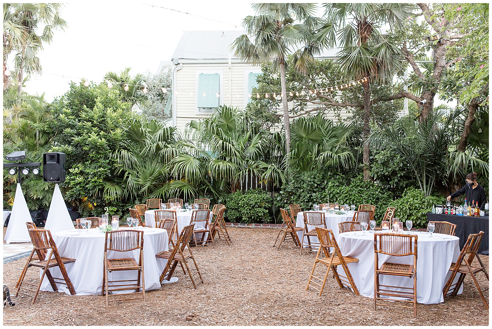 outdoor reception area with tables covered in white linens and wooden folding chairs at hemingway house