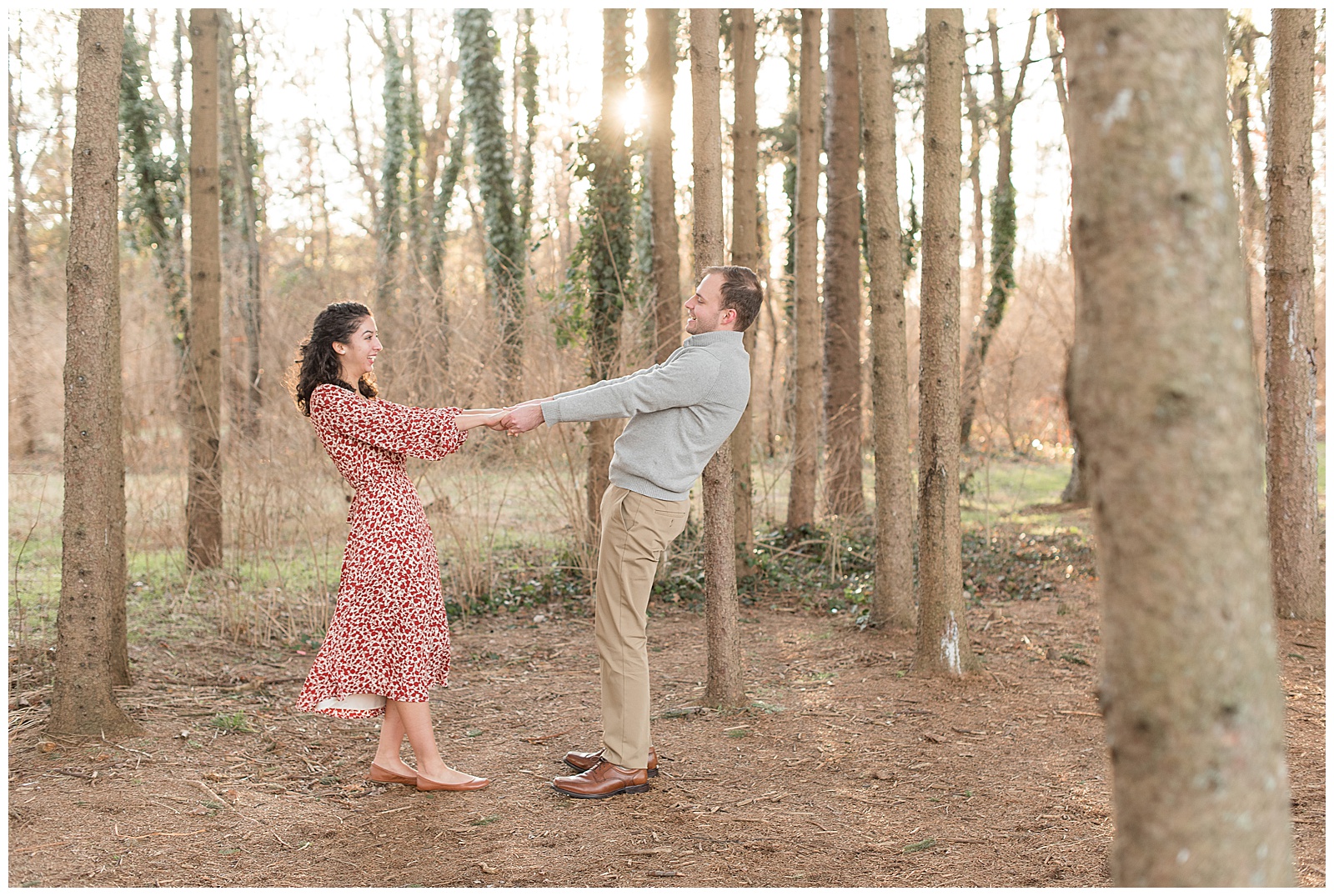 couple joins hands leaning apart from each other by trees with sun setting at overlook park